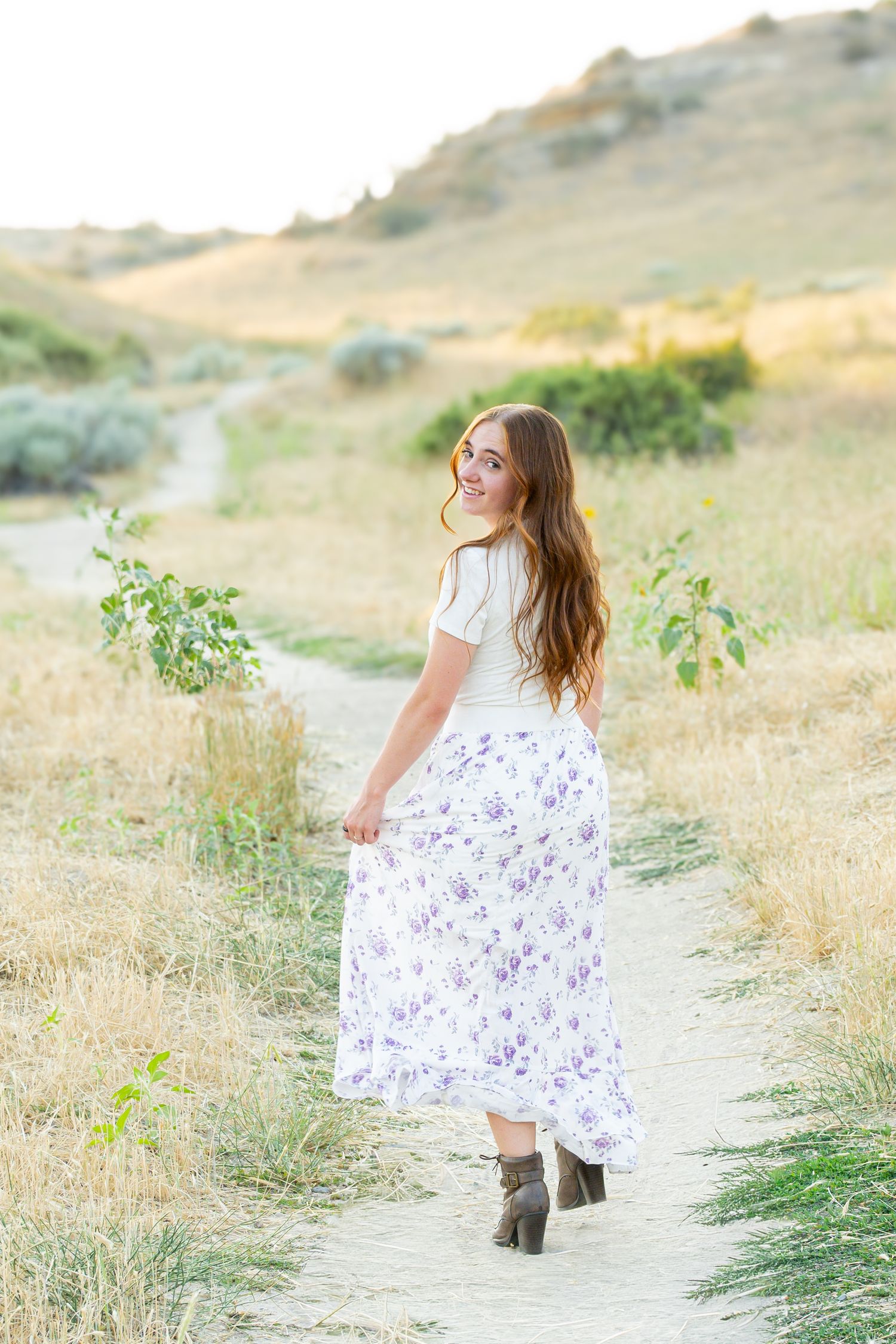 Woman in floral dress walks along winding path through golden summer field.
