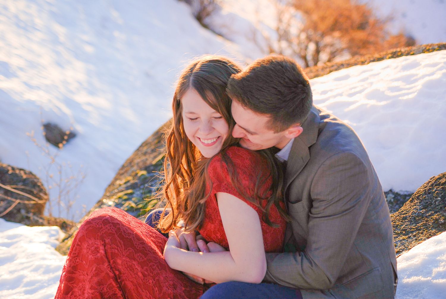 A couple shares tender moments in a snowy winter landscape at sunset with warm lighting.
