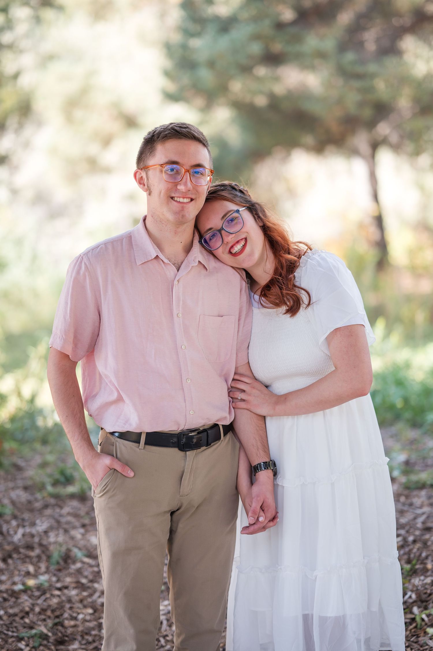 A couple in coordinated pink and white outfits share romantic moments while walking outdoors in a natural setting.
