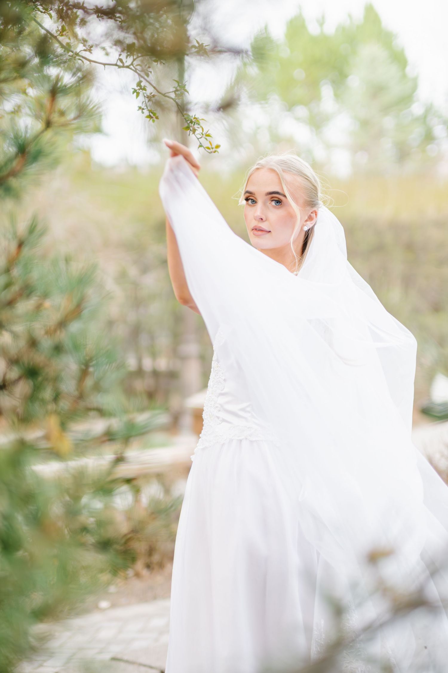 A woman wearing a white shawl stands among the trees, with a thoughtful expression on her face.