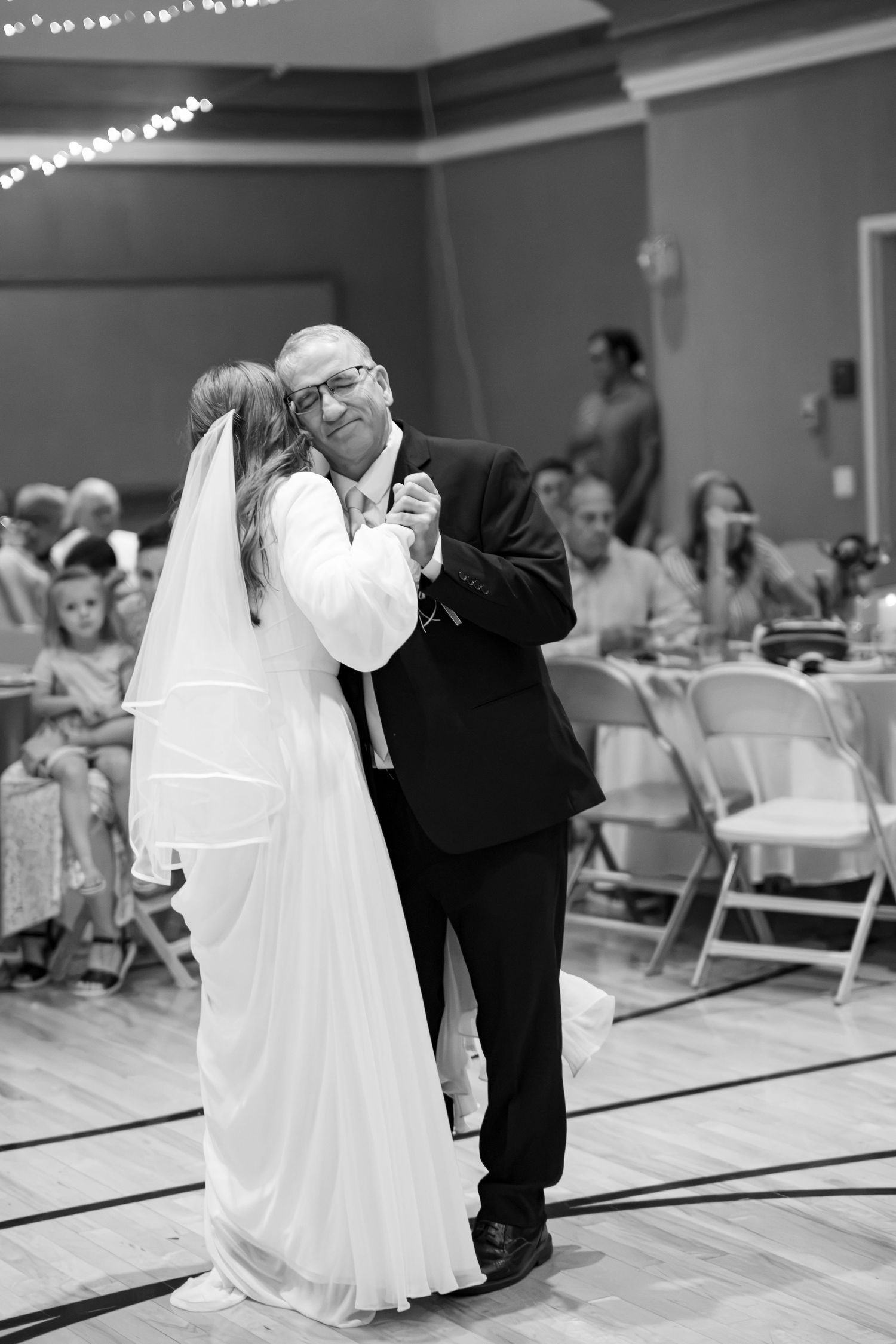 Black and white photo of bride sharing an emotional father-daughter dance at wedding reception.