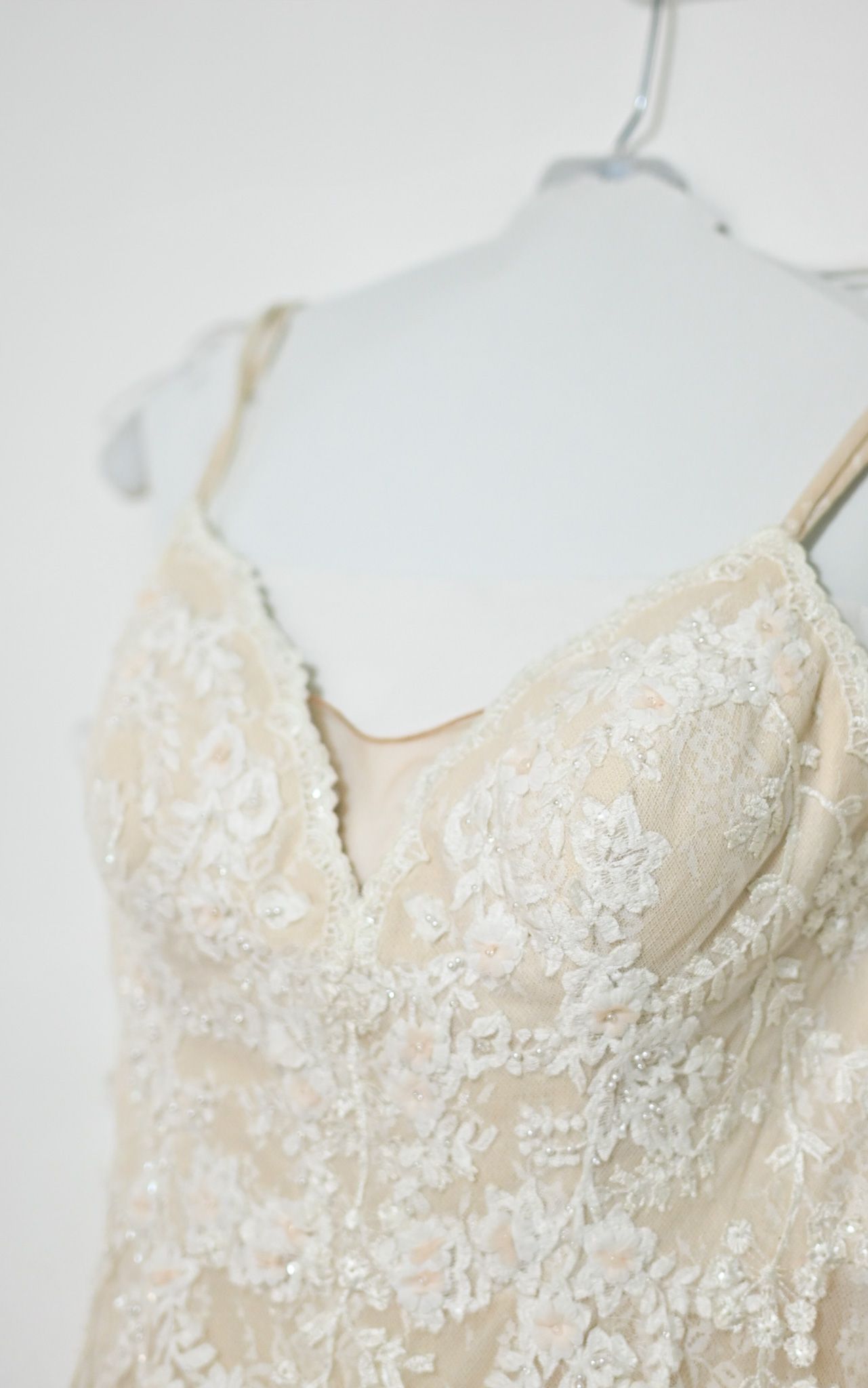 Close-up detail of delicate lace and beadwork on a champagne colored wedding dress.