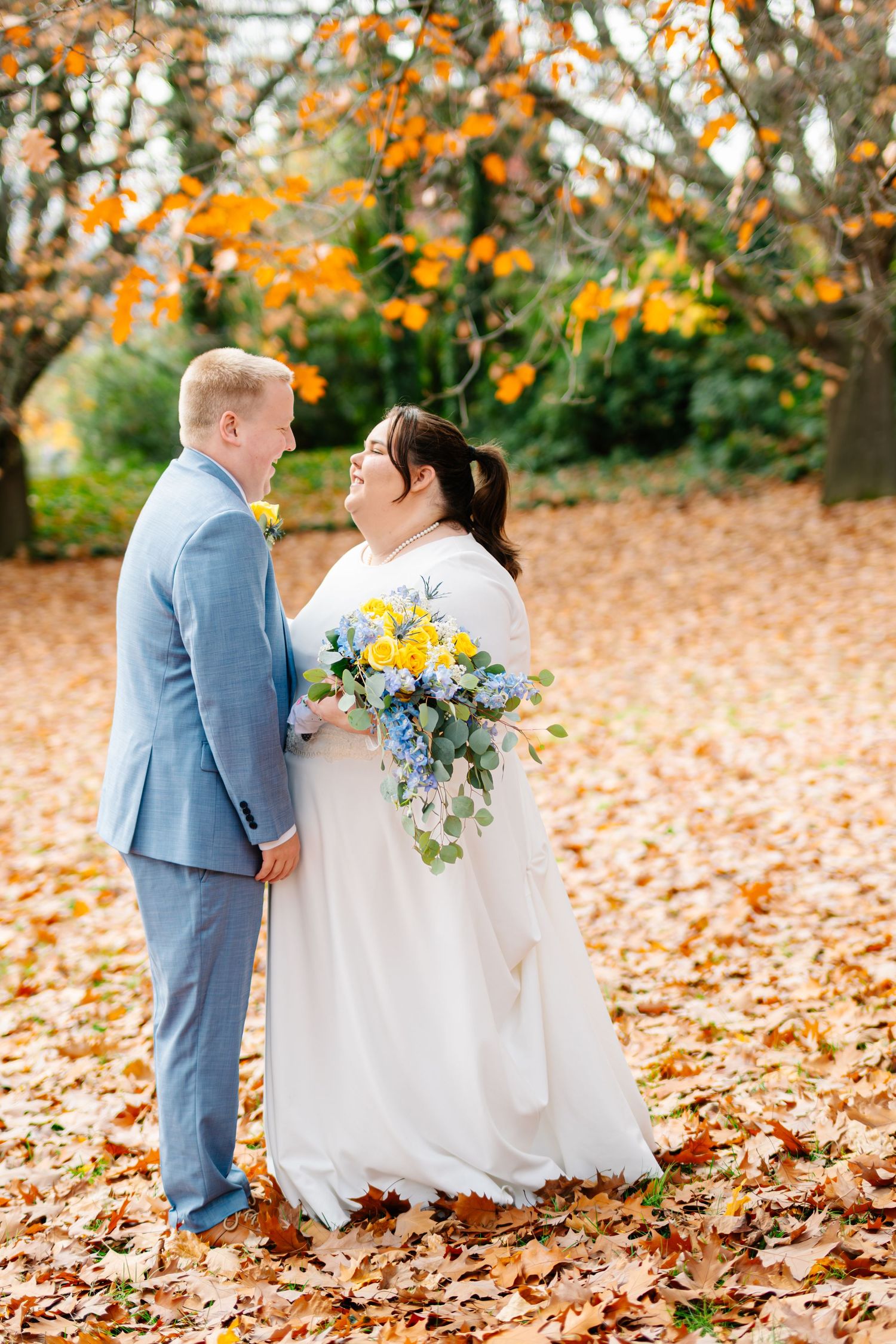 A couple shares an intimate moment surrounded by vibrant autumn leaves on their wedding day.