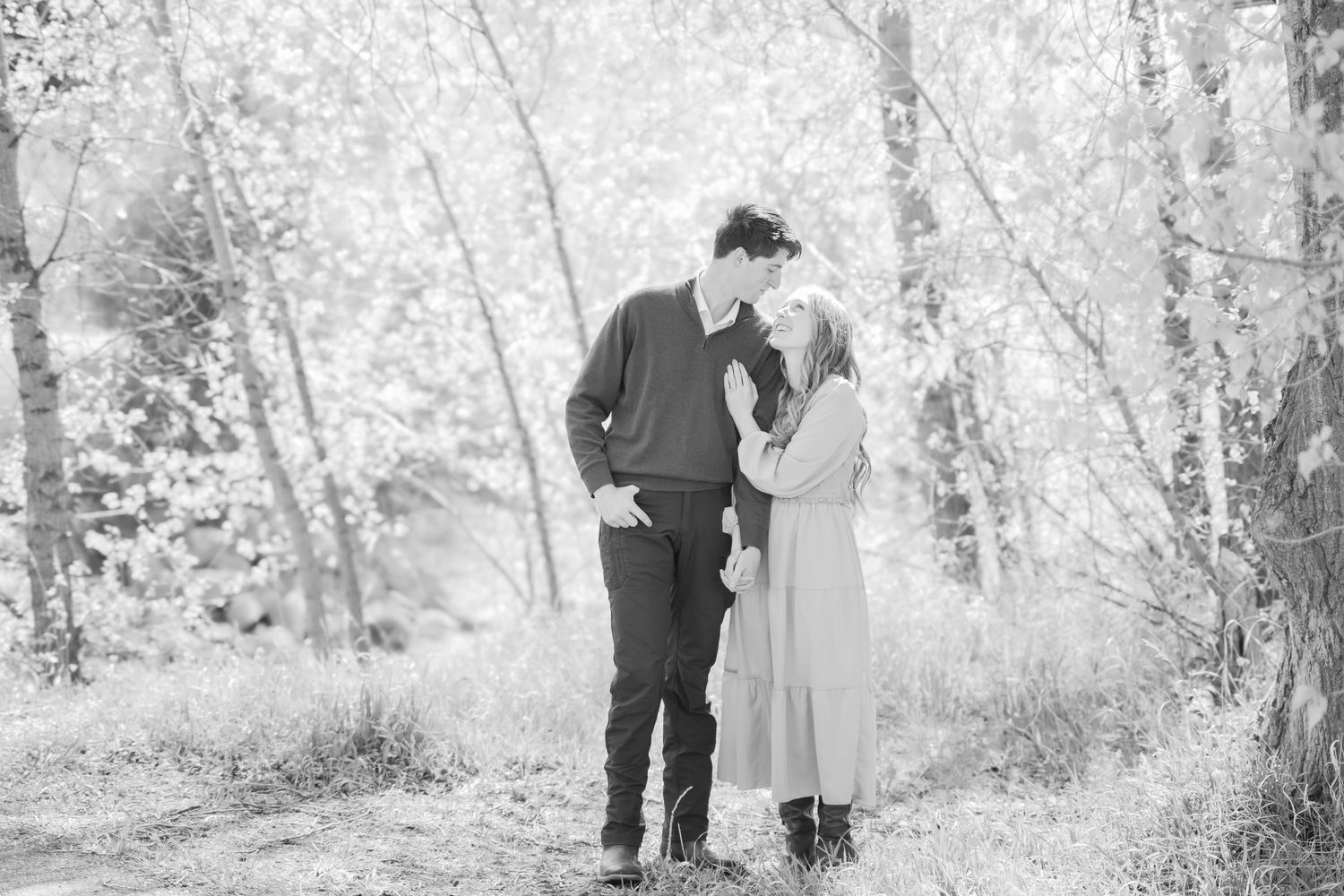 Black and white photo of a romantic couple sharing a tender moment in a forest setting.