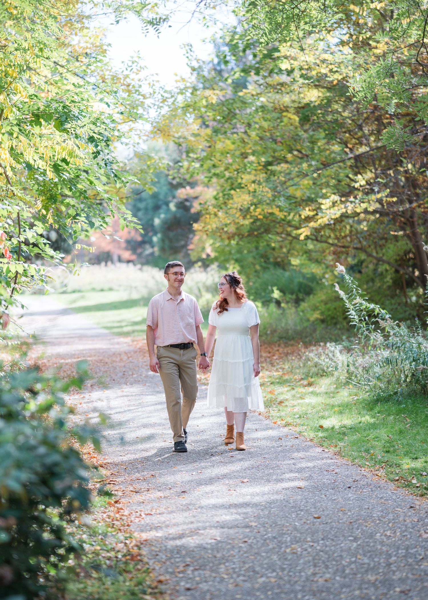 A couple strolls hand in hand down a peaceful tree-lined gravel path on an autumn day.