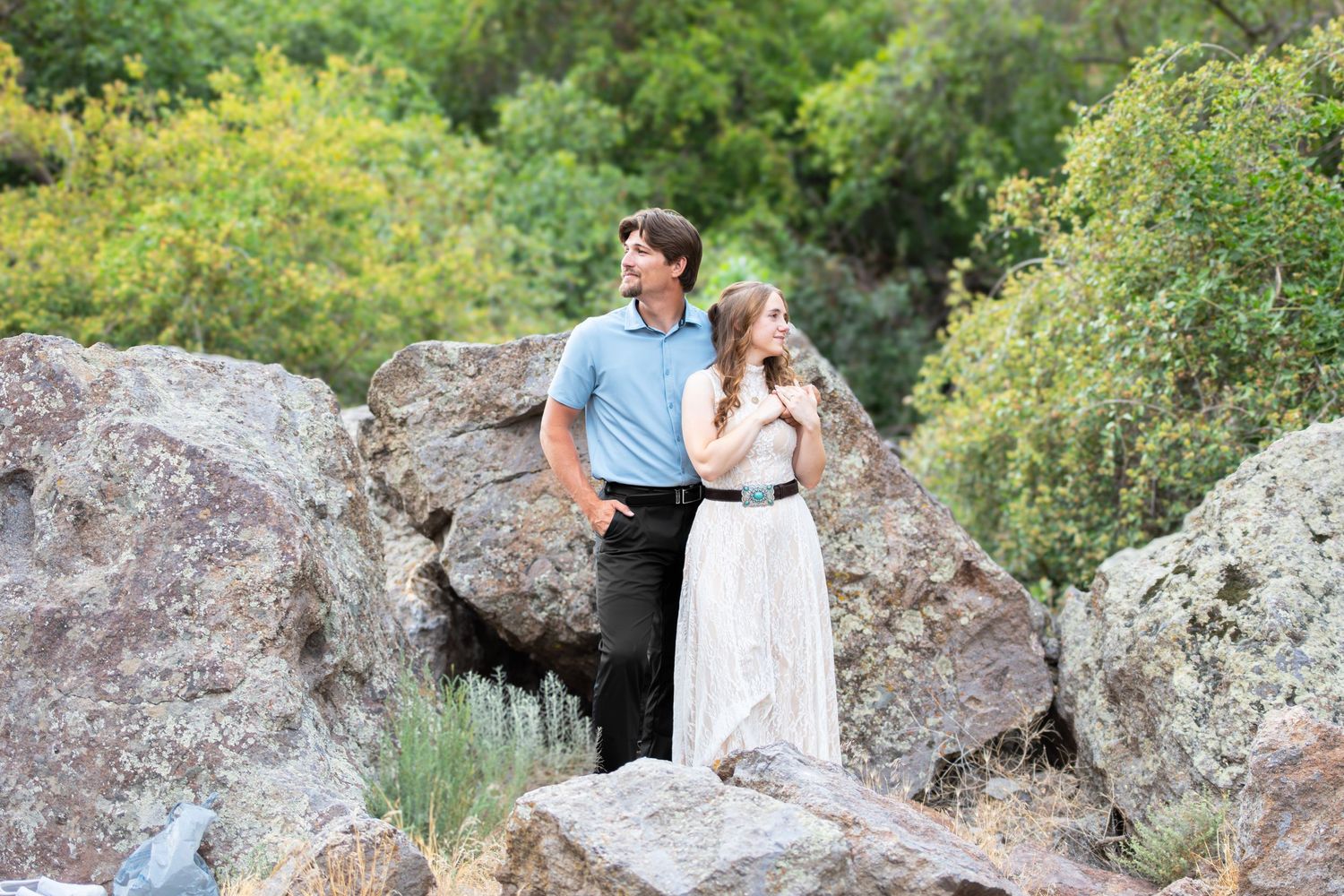 Couple standing on rocky boulders surrounded by lush green trees in an outdoor nature setting.