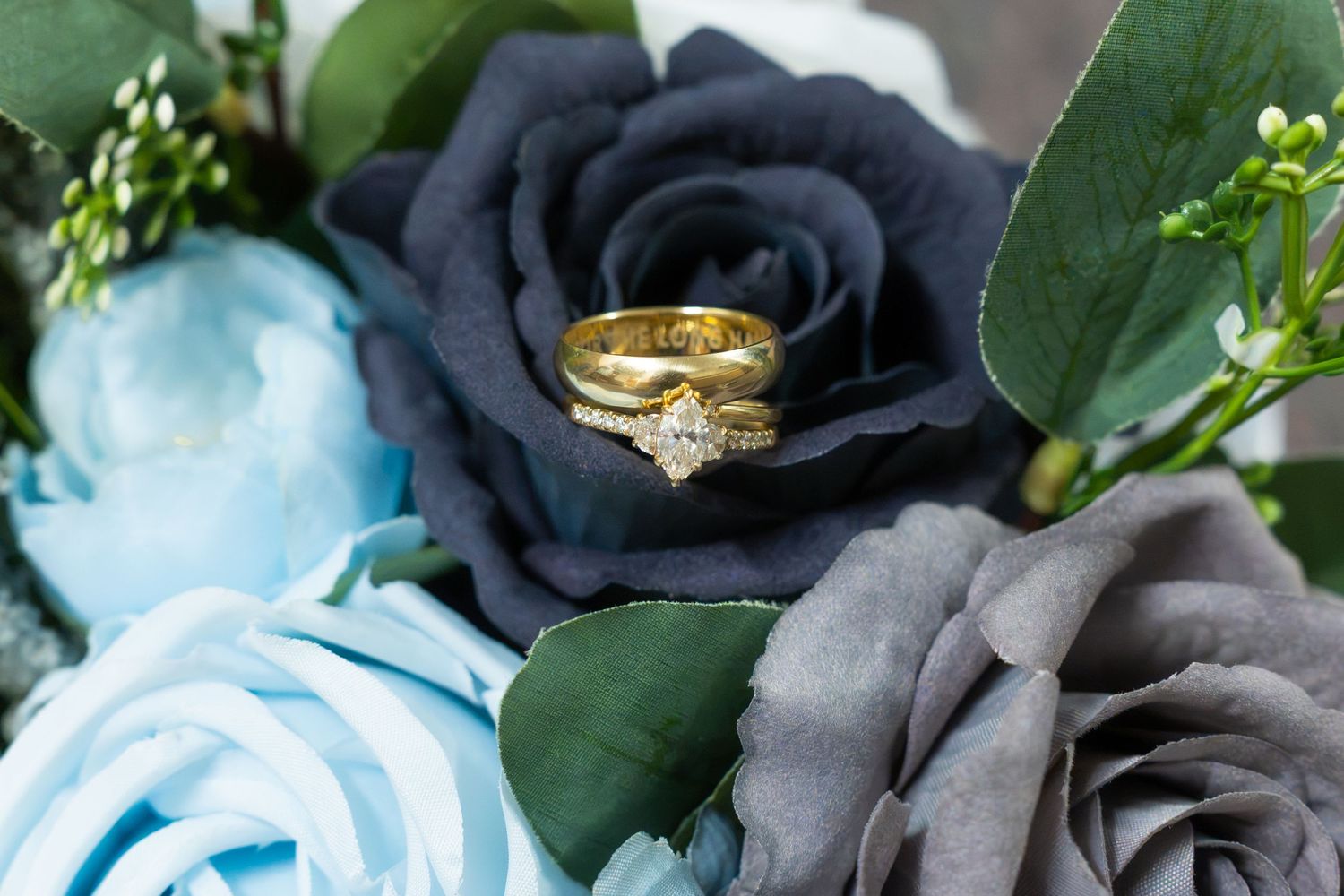 Gold diamond engagement ring and wedding band nestled in blue and gray roses bouquet.