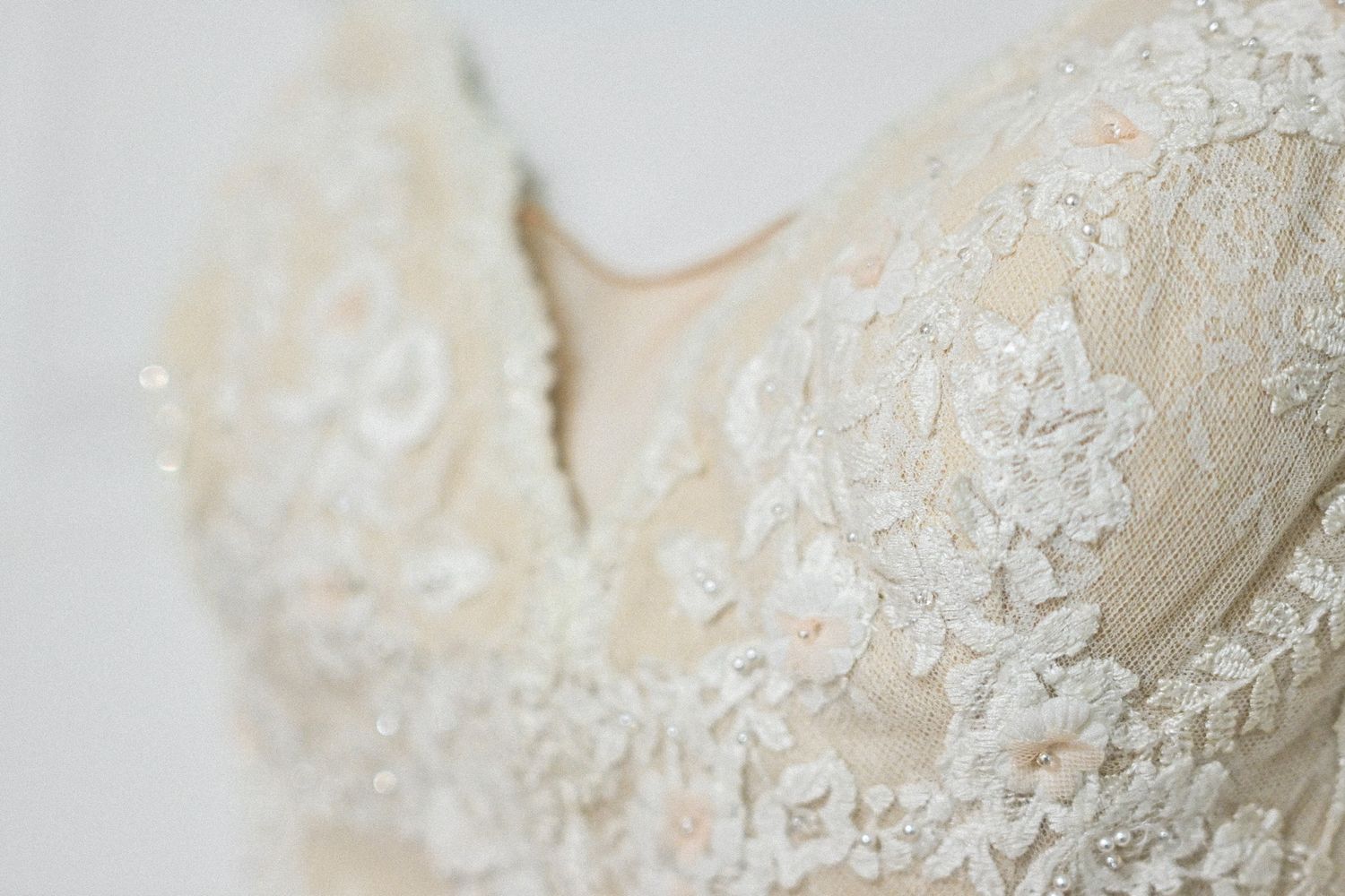 Close-up detail of delicate white lace and beadwork on a wedding dress bodice.