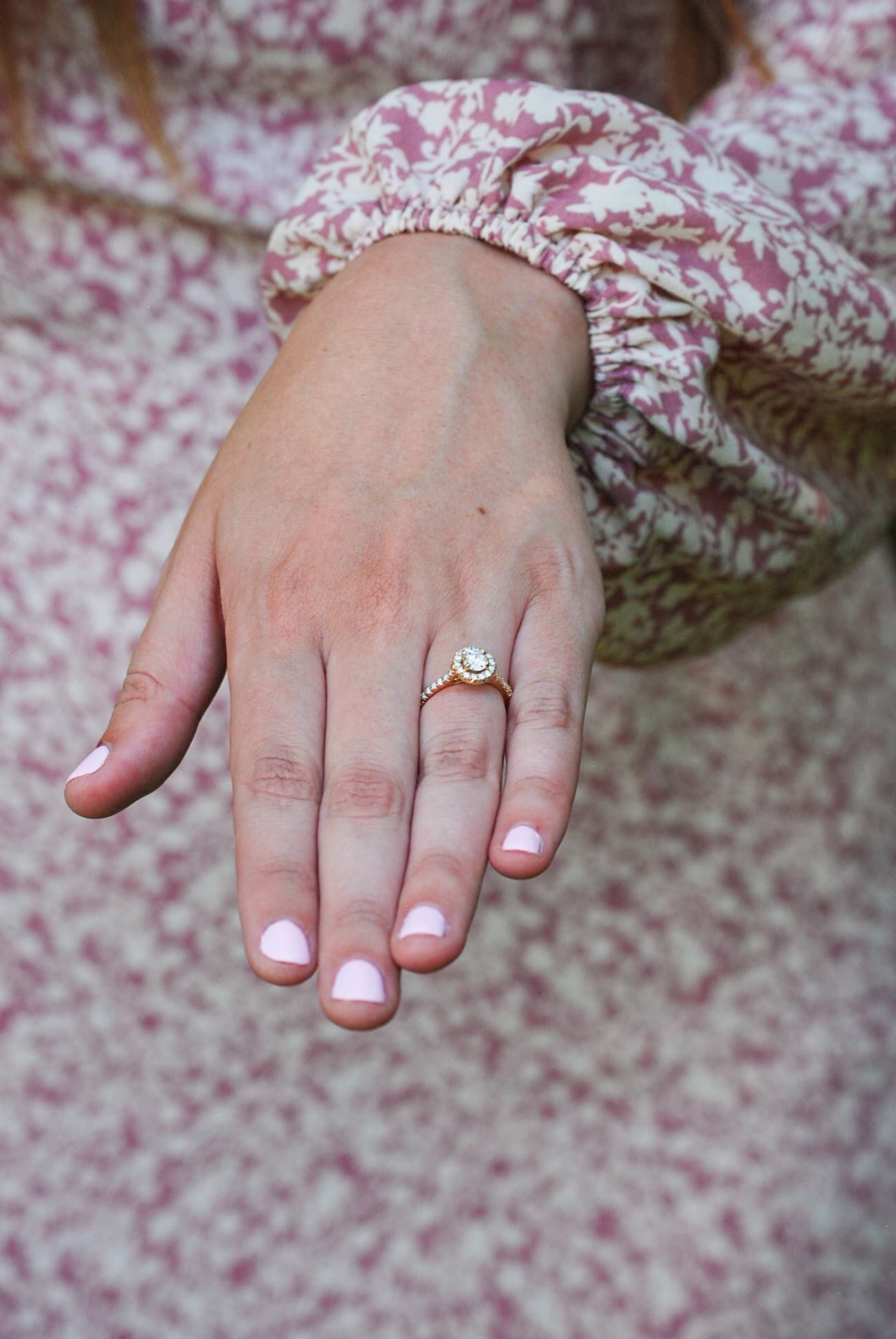 Close-up sequence showing a delicate engagement ring on a woman's hand against a pink floral background.