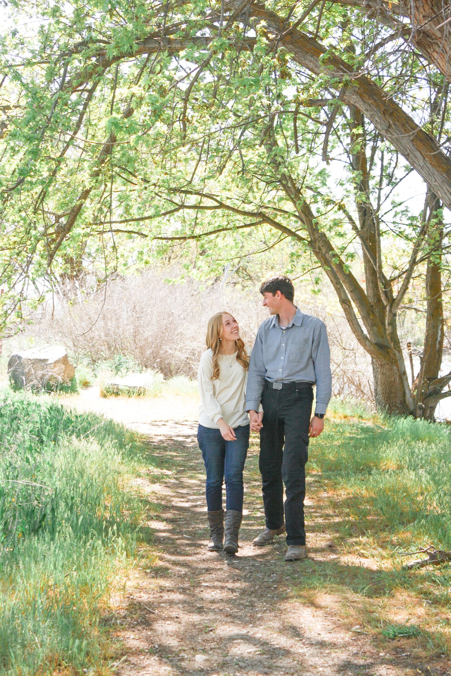 A couple walks hand in hand along a tree-lined path during an outdoor photoshoot.