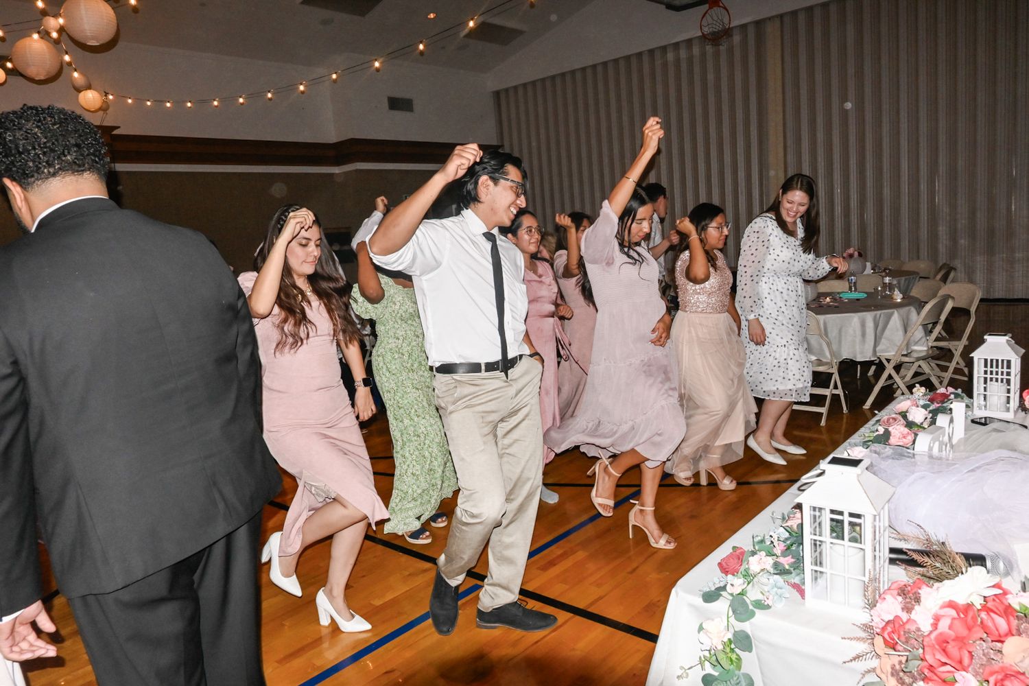 Wedding reception dance floor filled with guests celebrating and dancing under string lights.