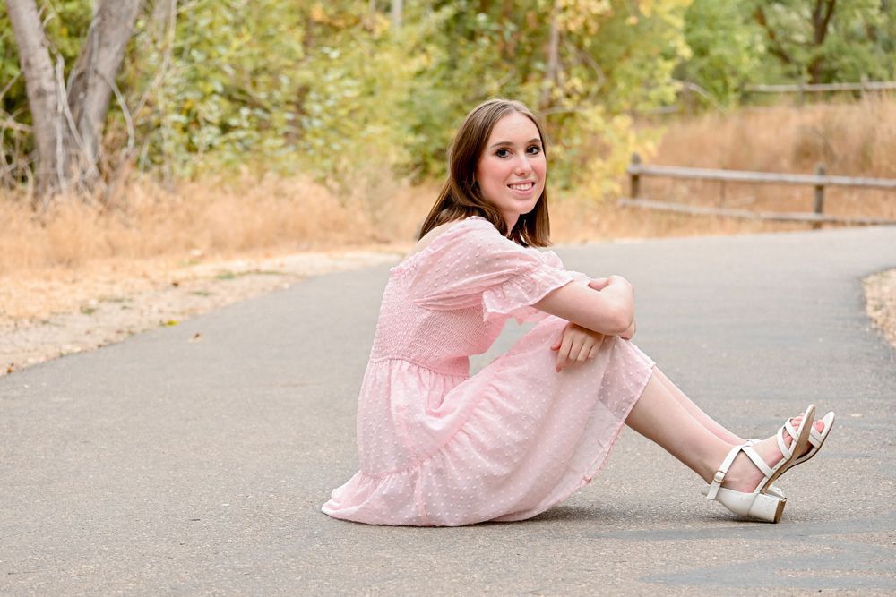 A ballet dancer in a pink tulle dress performs graceful poses on a paved path in an outdoor setting.