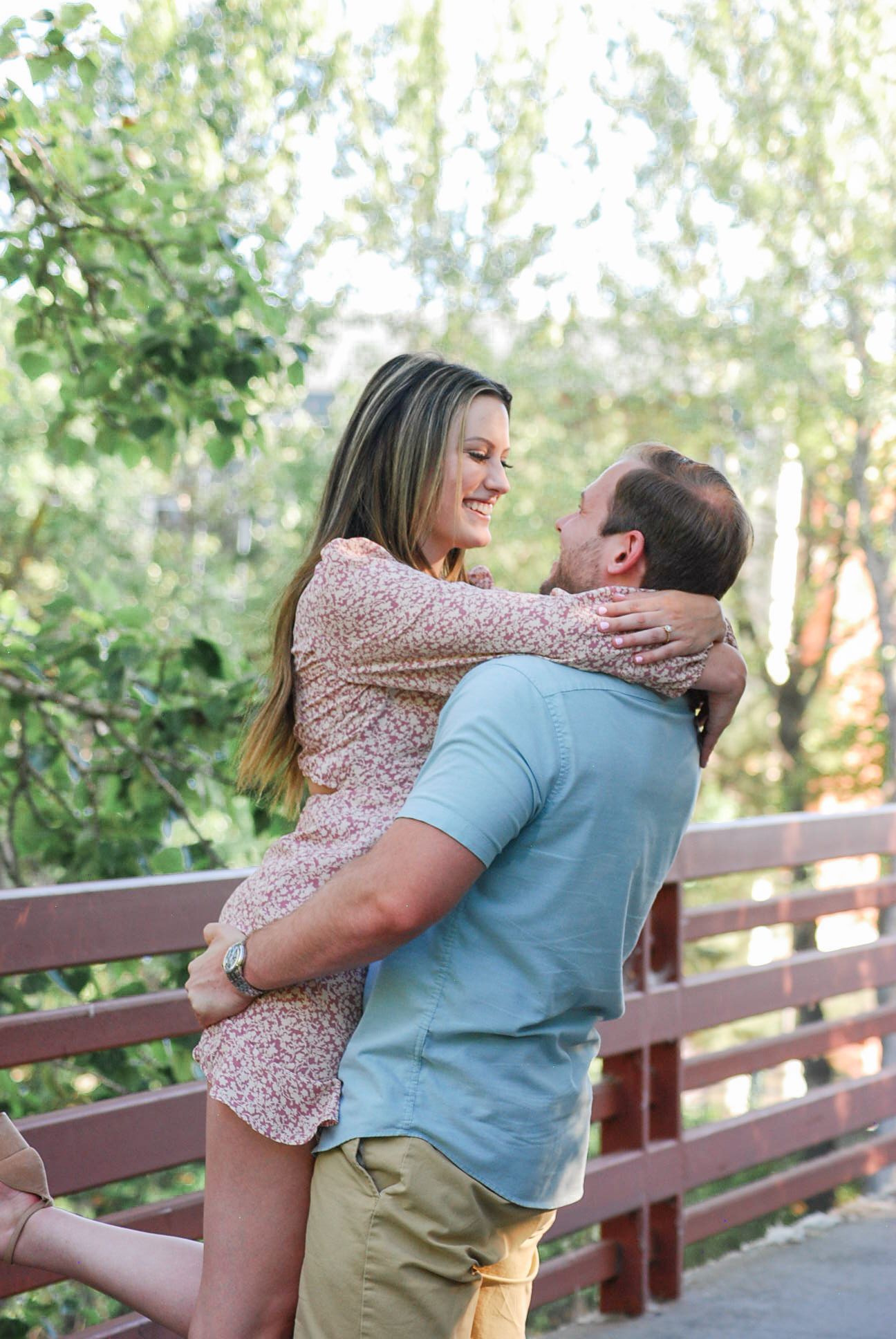 Romantic couple embracing and lifting on a wooden deck surrounded by lush greenery.