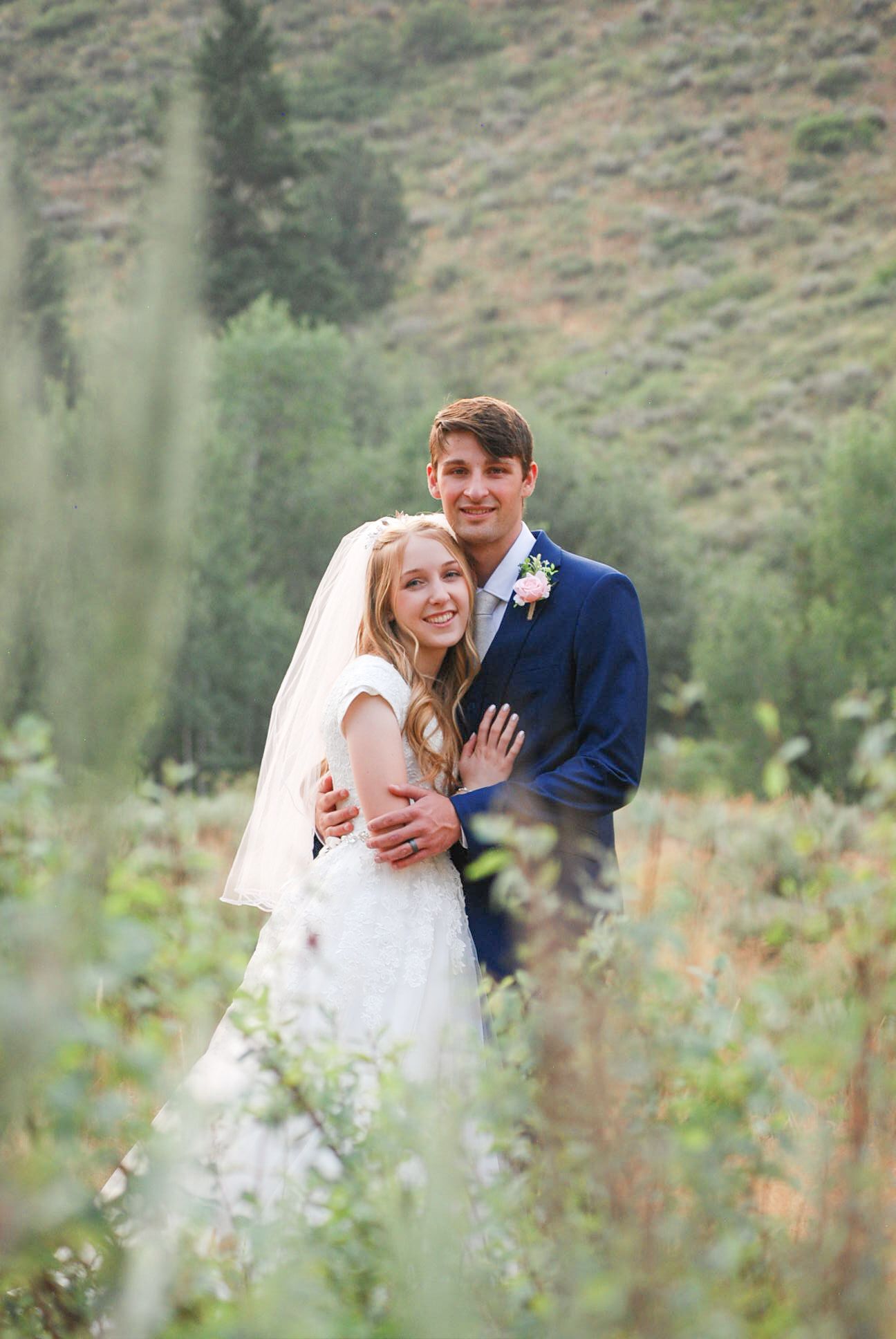 Newlyweds share intimate moments in mountain meadow with flowing bridal veil.