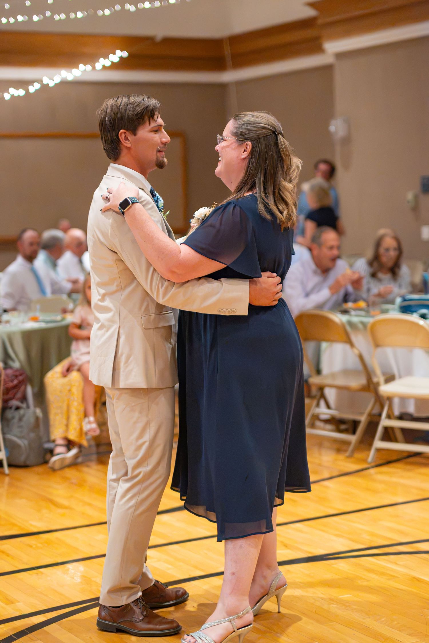 Couple sharing a first dance at wedding reception in elegant venue, groom in tan suit, bride in navy dress.