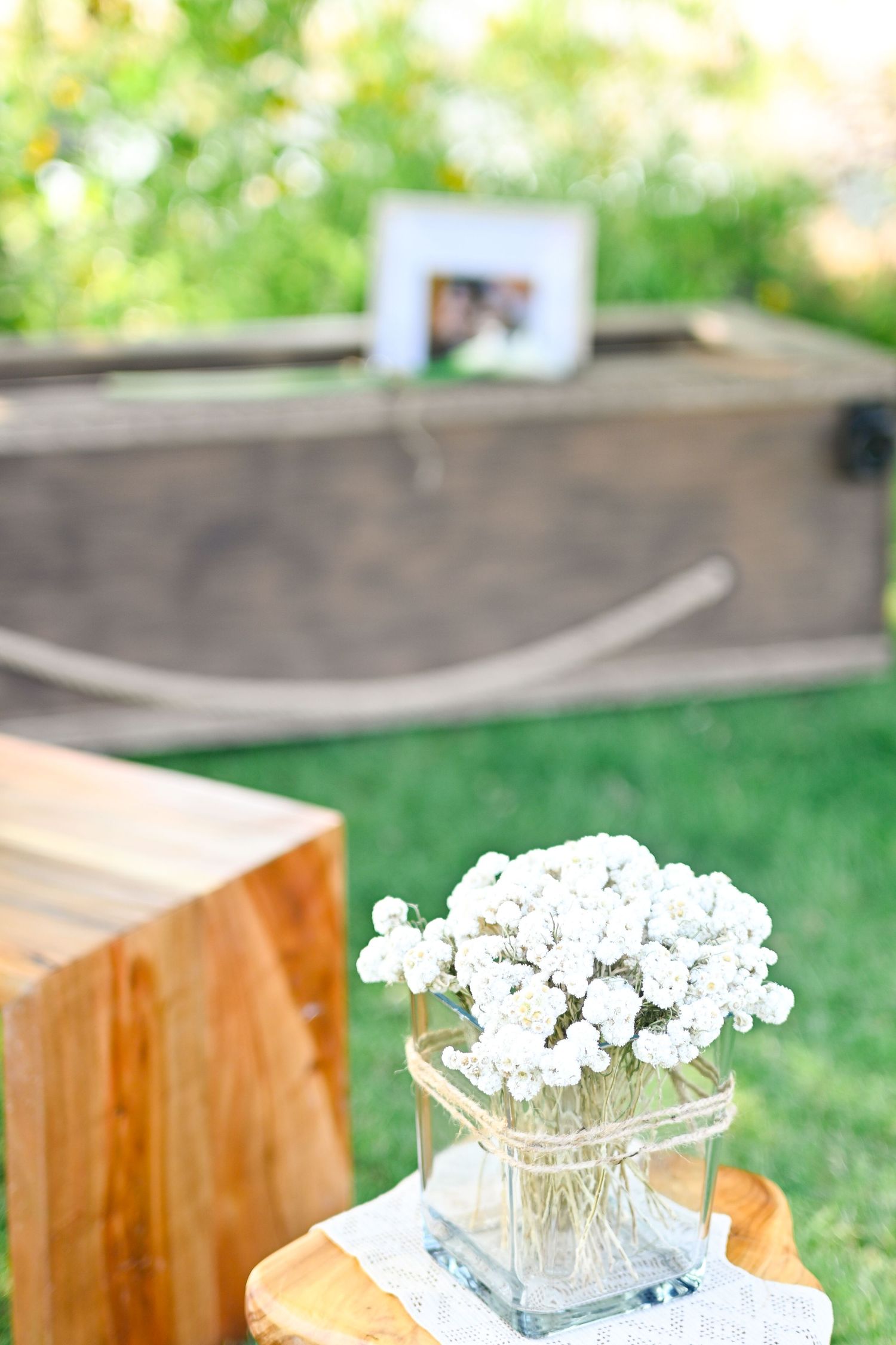 Small glass vase with delicate white baby's breath flowers sits on wooden surface in outdoor garden setting.