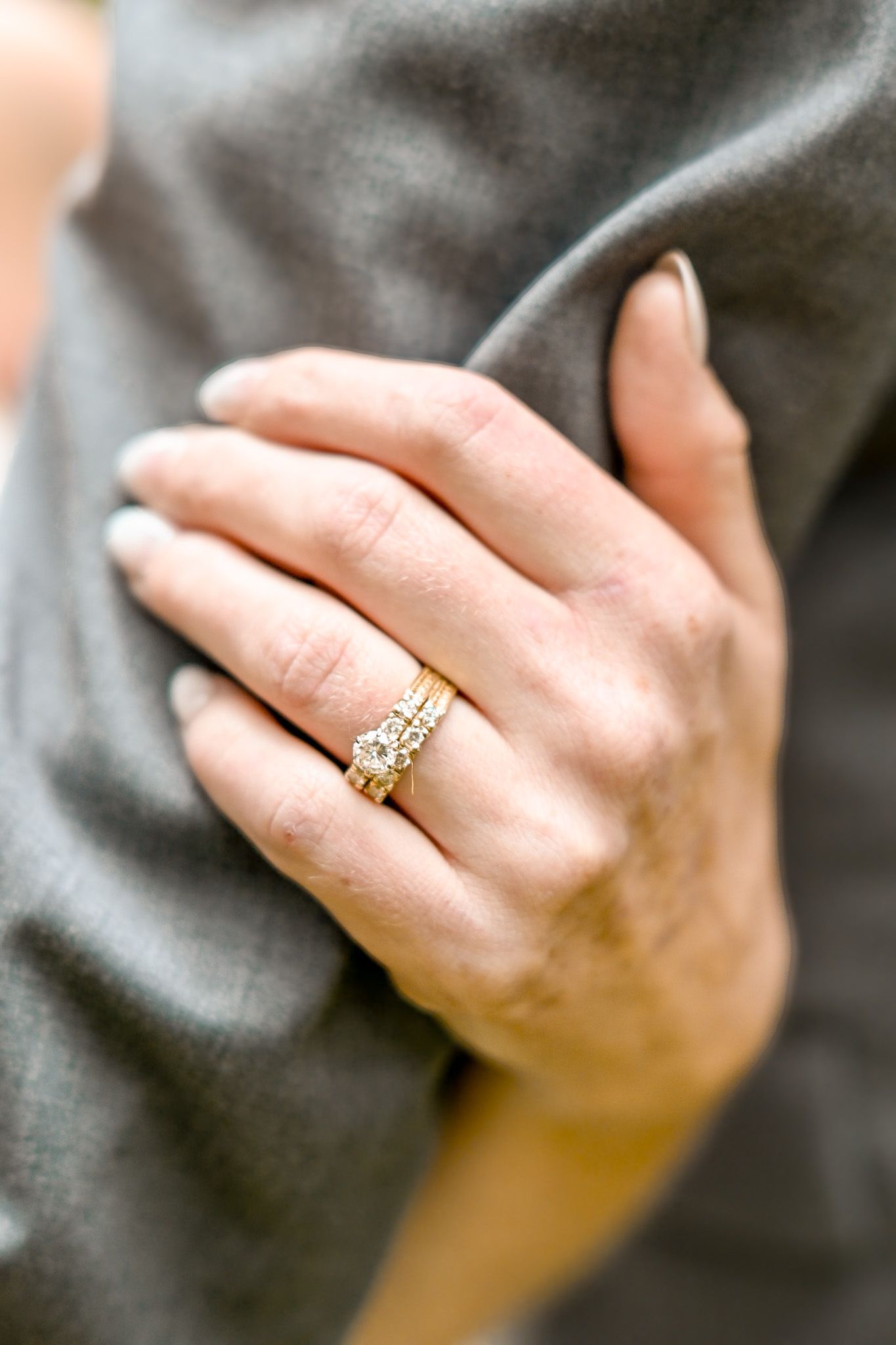 Gold engagement ring detail shot on gray fabric background.