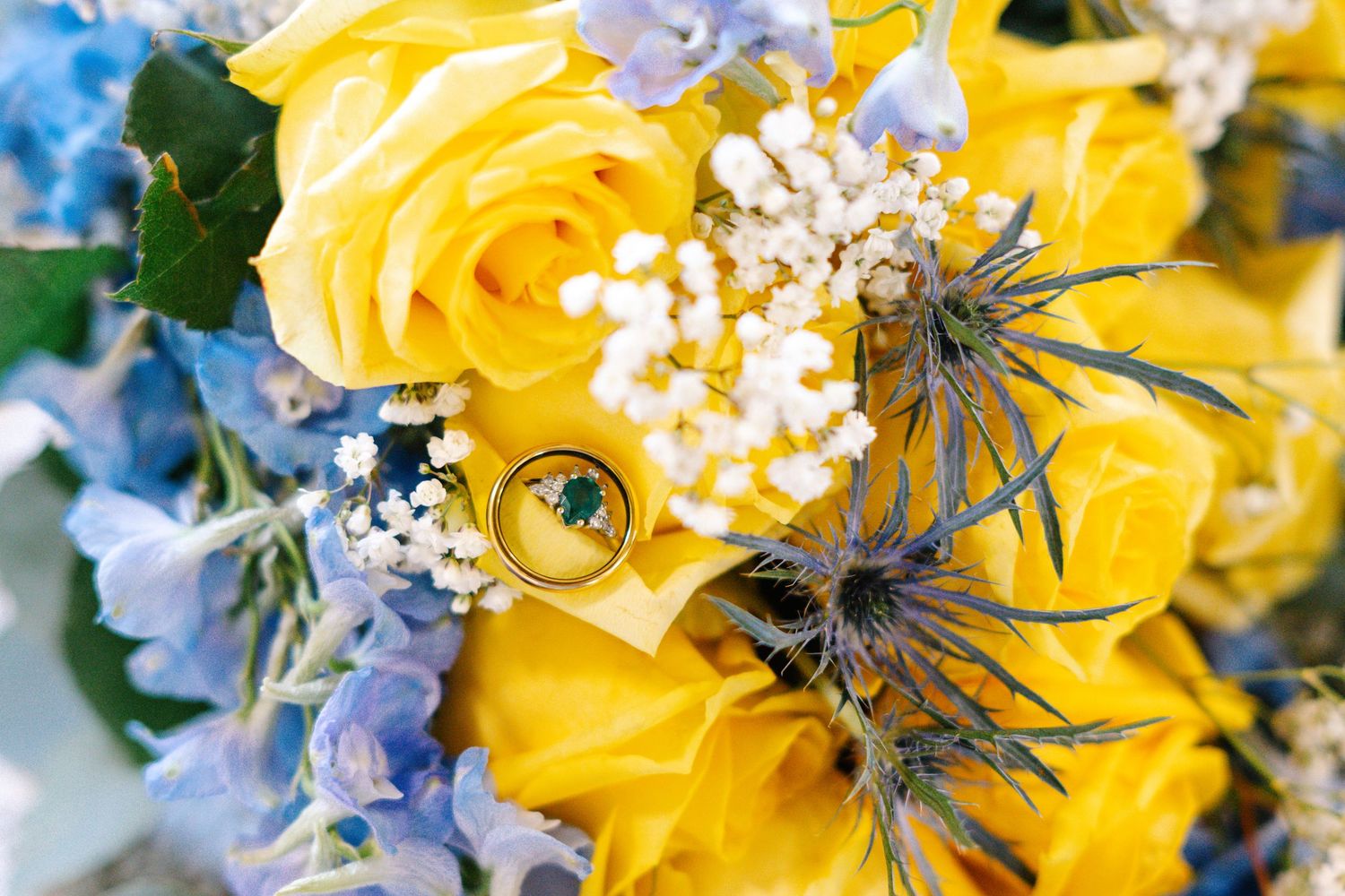 Close-up of yellow roses and blue hydrangeas in a wedding bouquet with delicate white baby's breath accents.