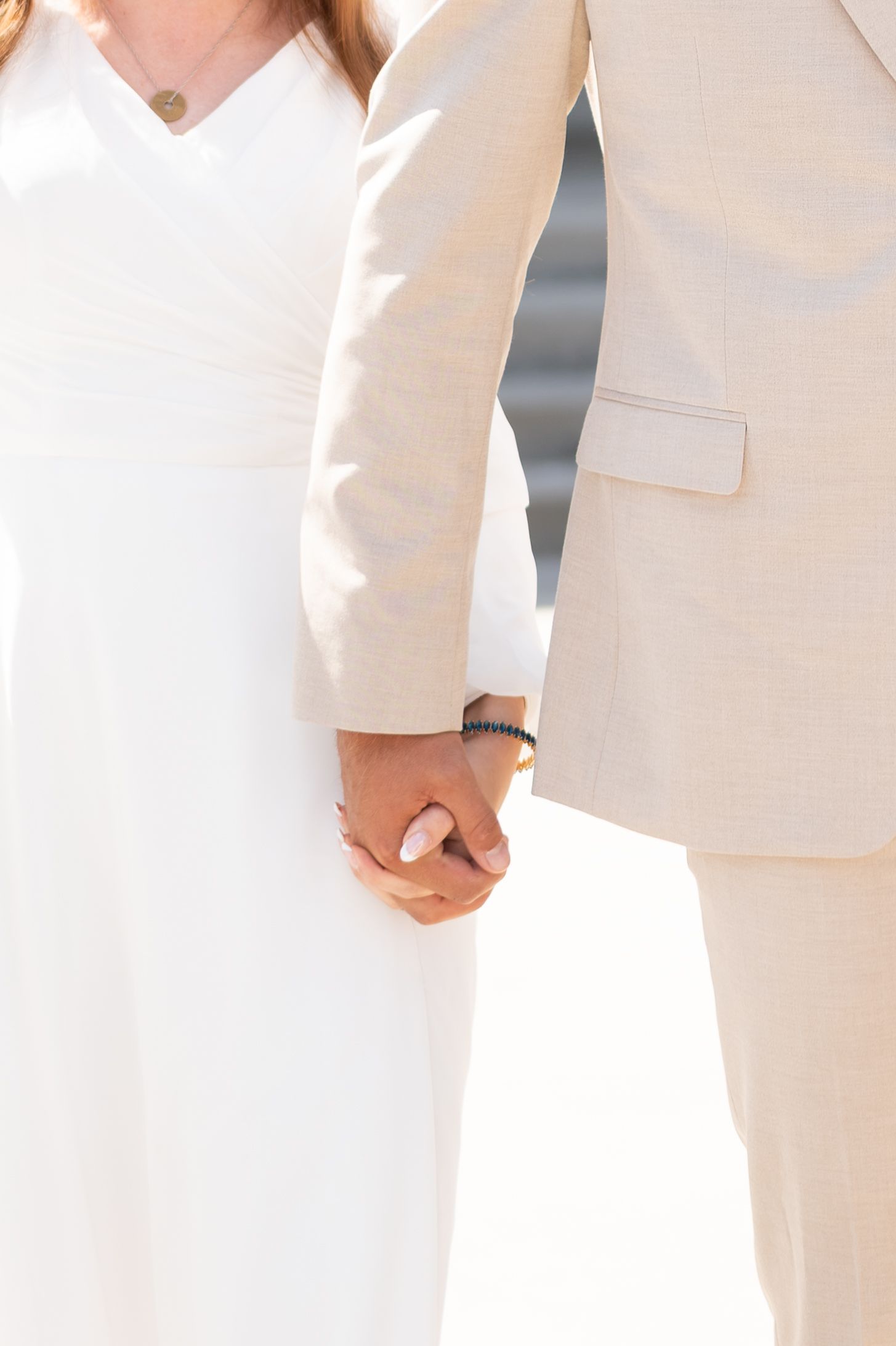 Bride in white dress and groom in beige suit holding hands at wedding ceremony.