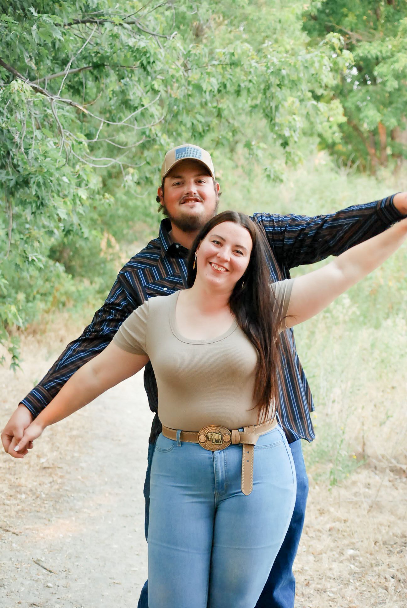 A playful couple poses with outstretched arms in a natural outdoor setting.