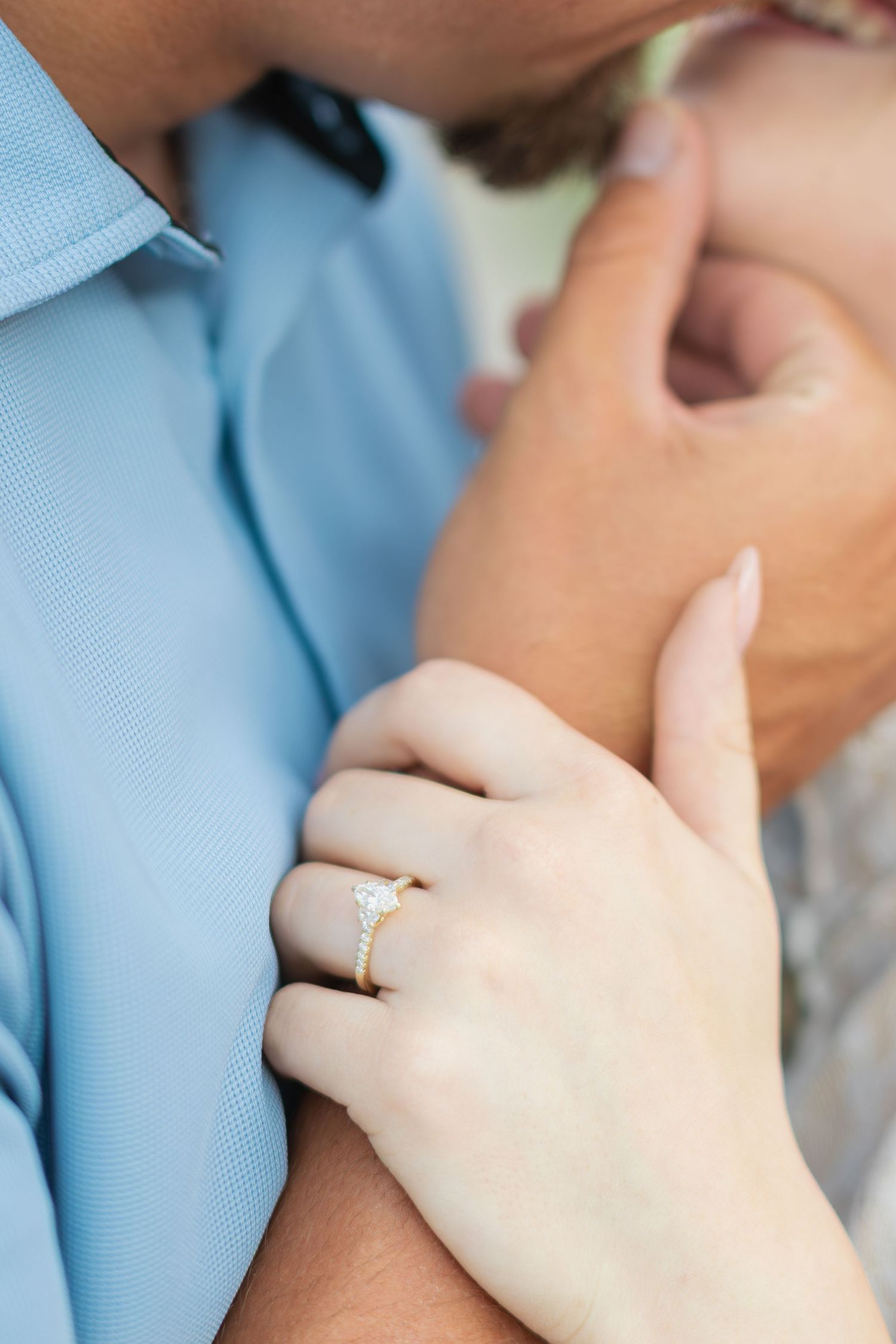 Close-up of a woman's hand with a gold diamond engagement ring resting on a man's arm as they share a romantic moment.