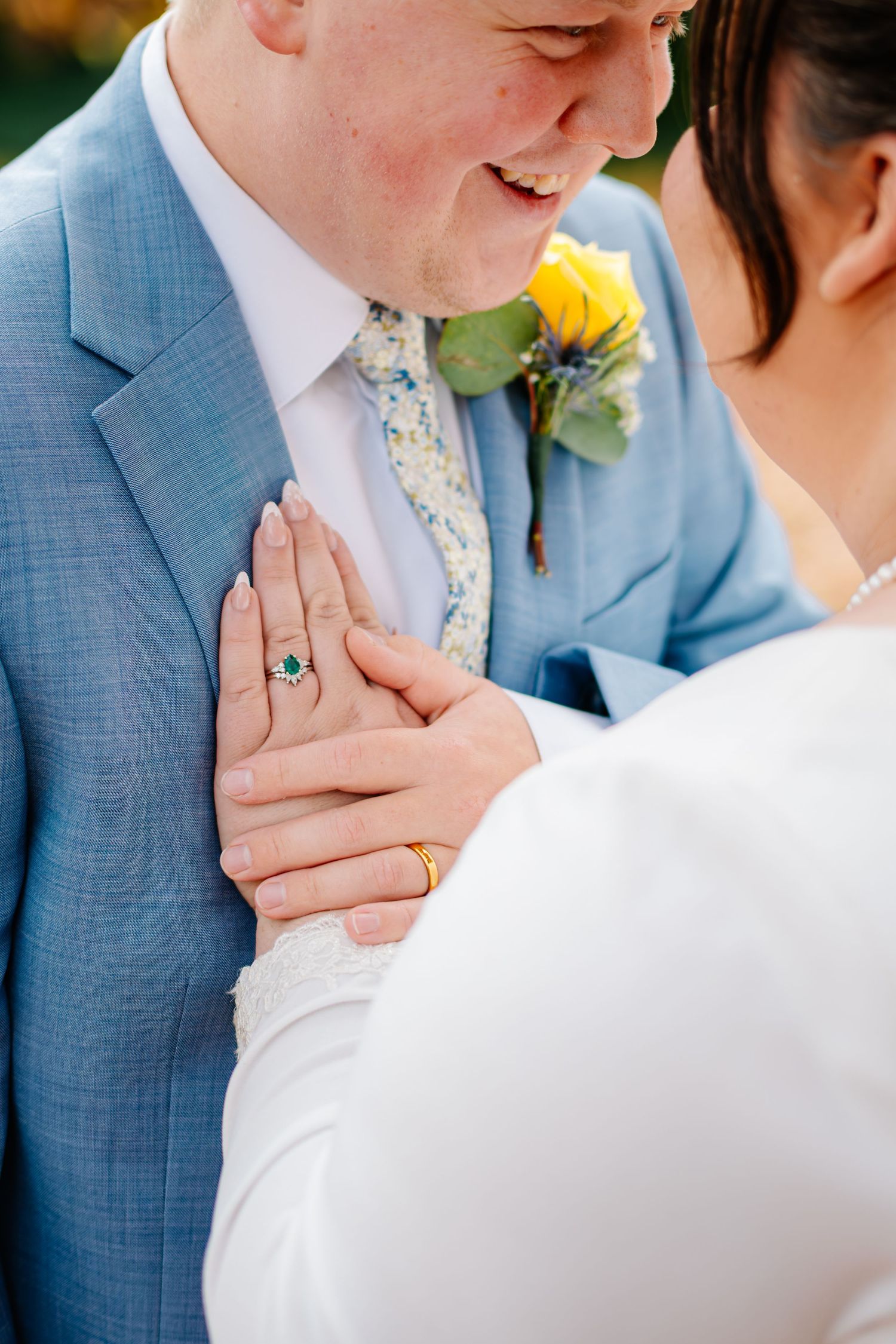 Close-up wedding photo showing couple's hands with rings during an intimate moment in blue and white attire.