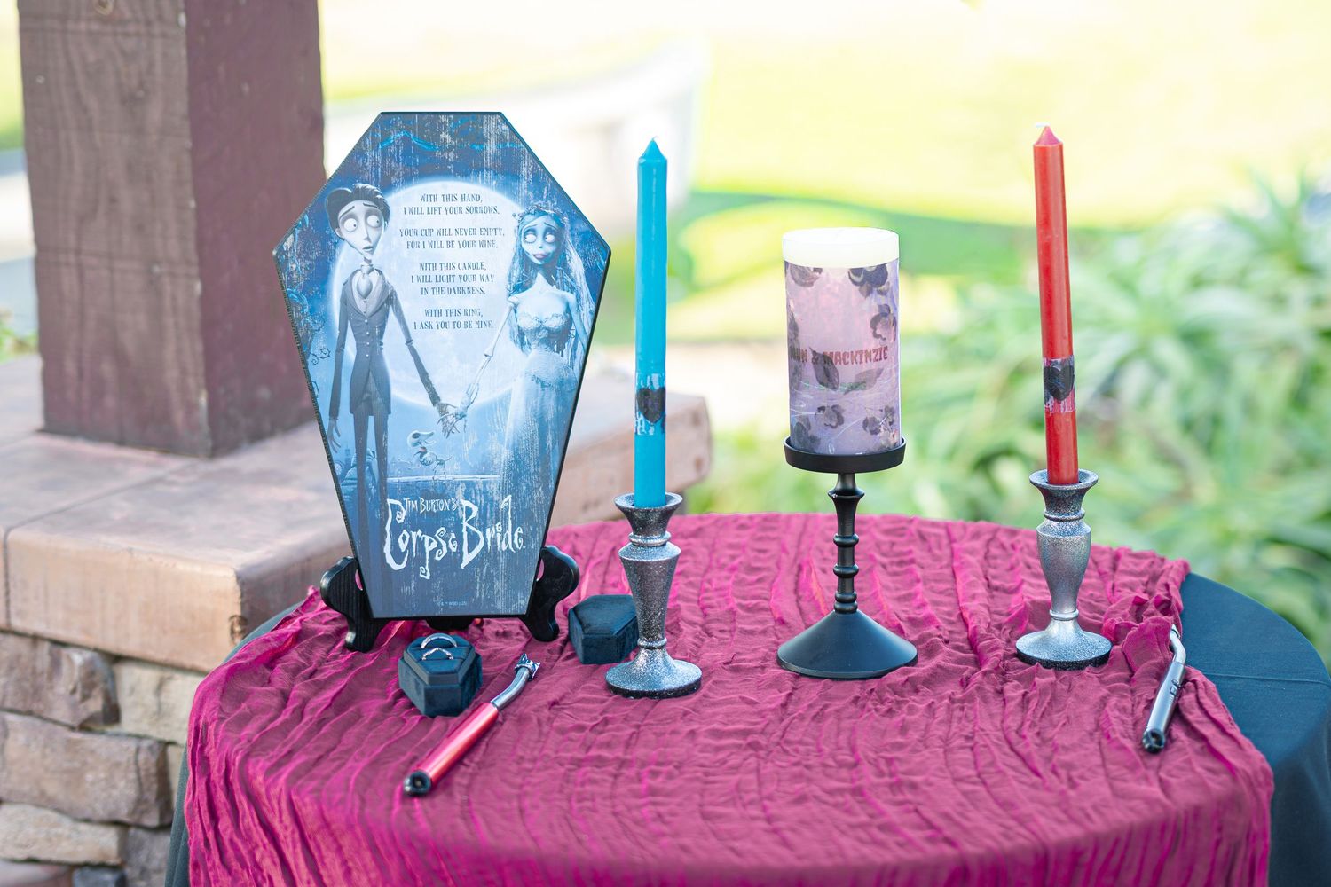Corpse Bride themed wedding table with coffin sign, blue and red candles on burgundy tablecloth.