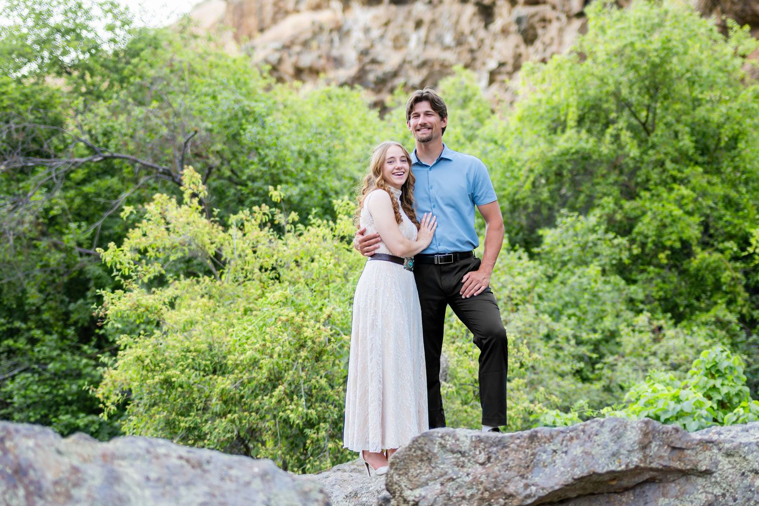 Couple posing on rocks surrounded by lush green trees in an outdoor engagement photo session.