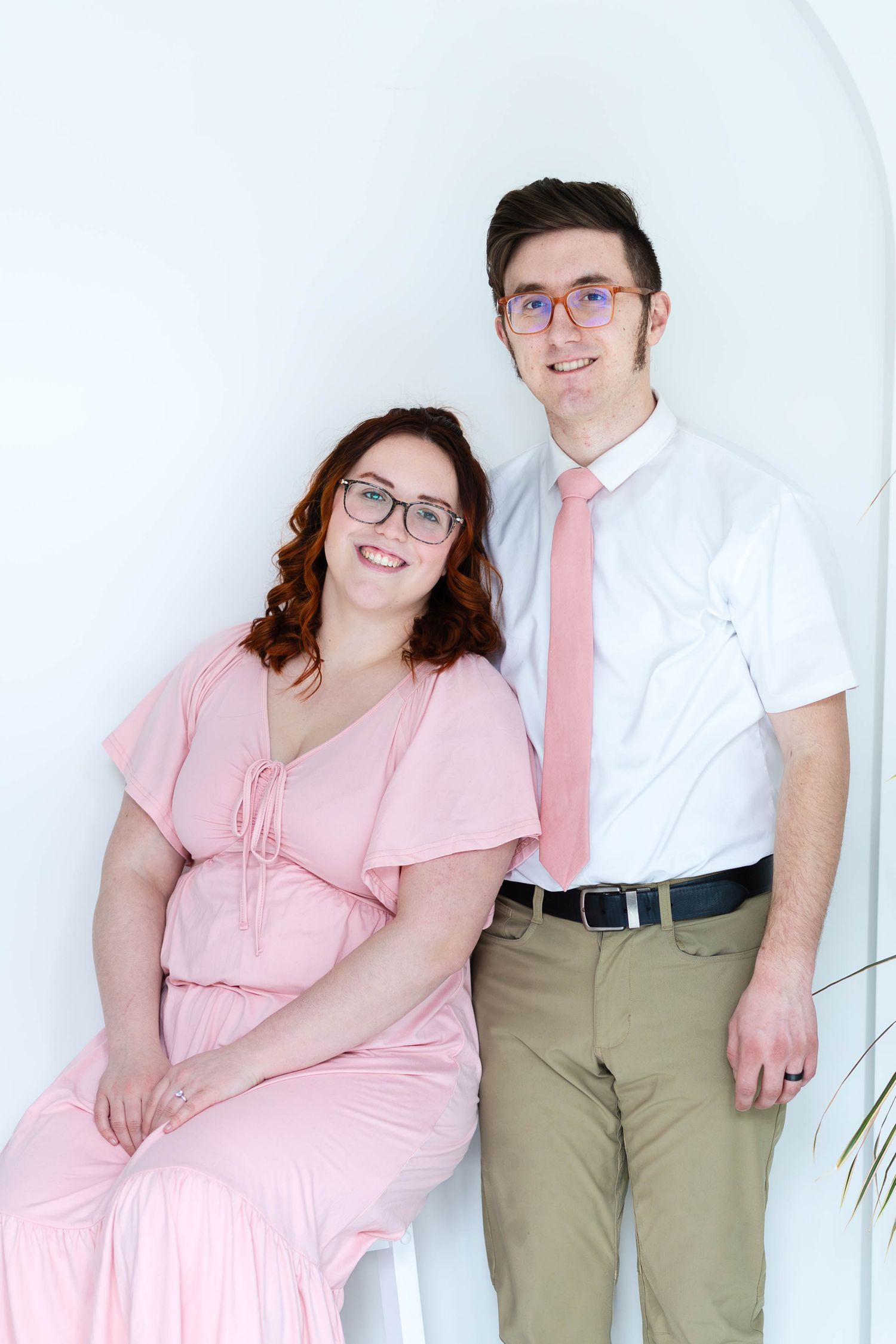 A couple wearing coordinated pink and white outfits pose together against a white backdrop for a formal portrait.