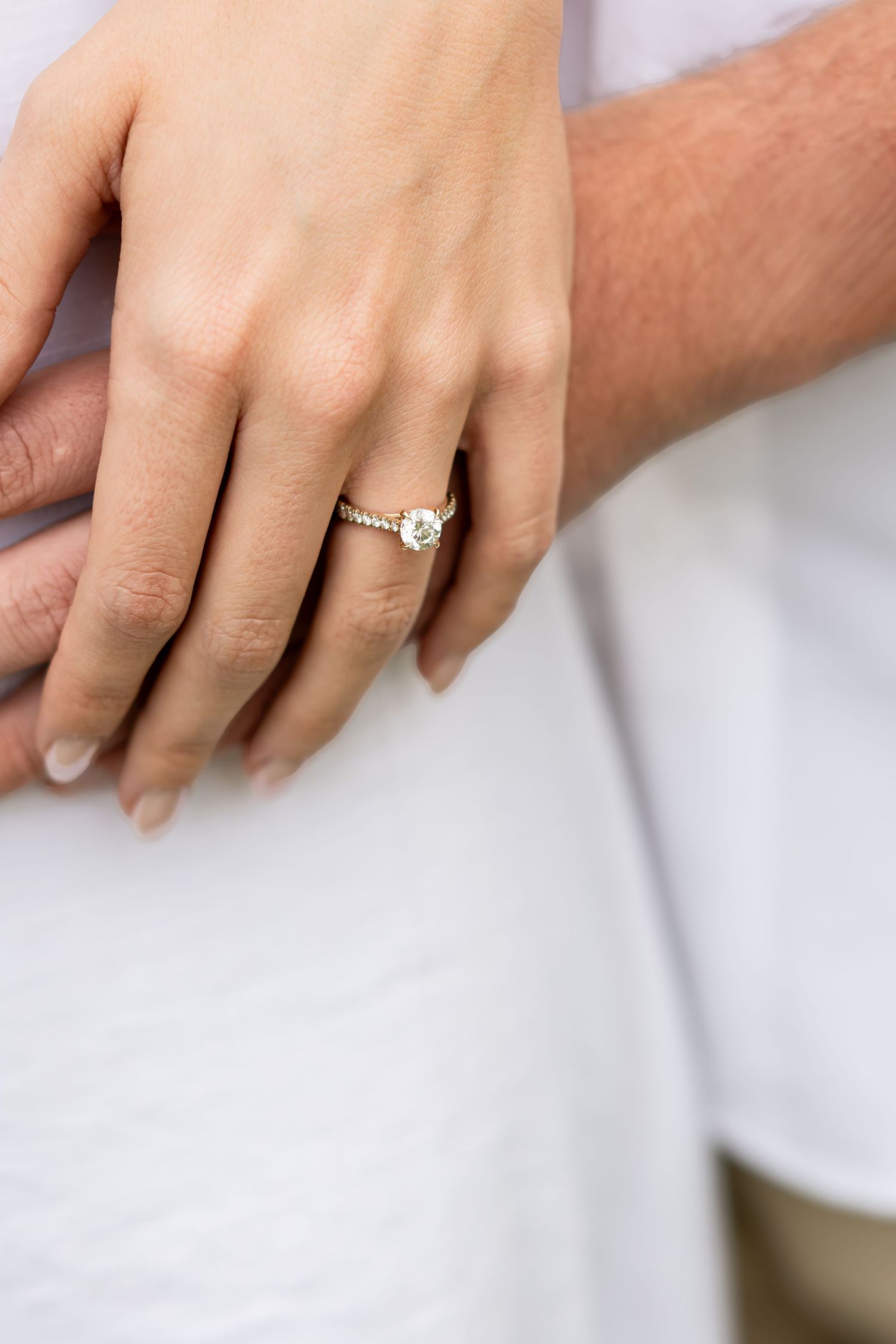 Close-up of hands showing delicate engagement ring against white fabric background.