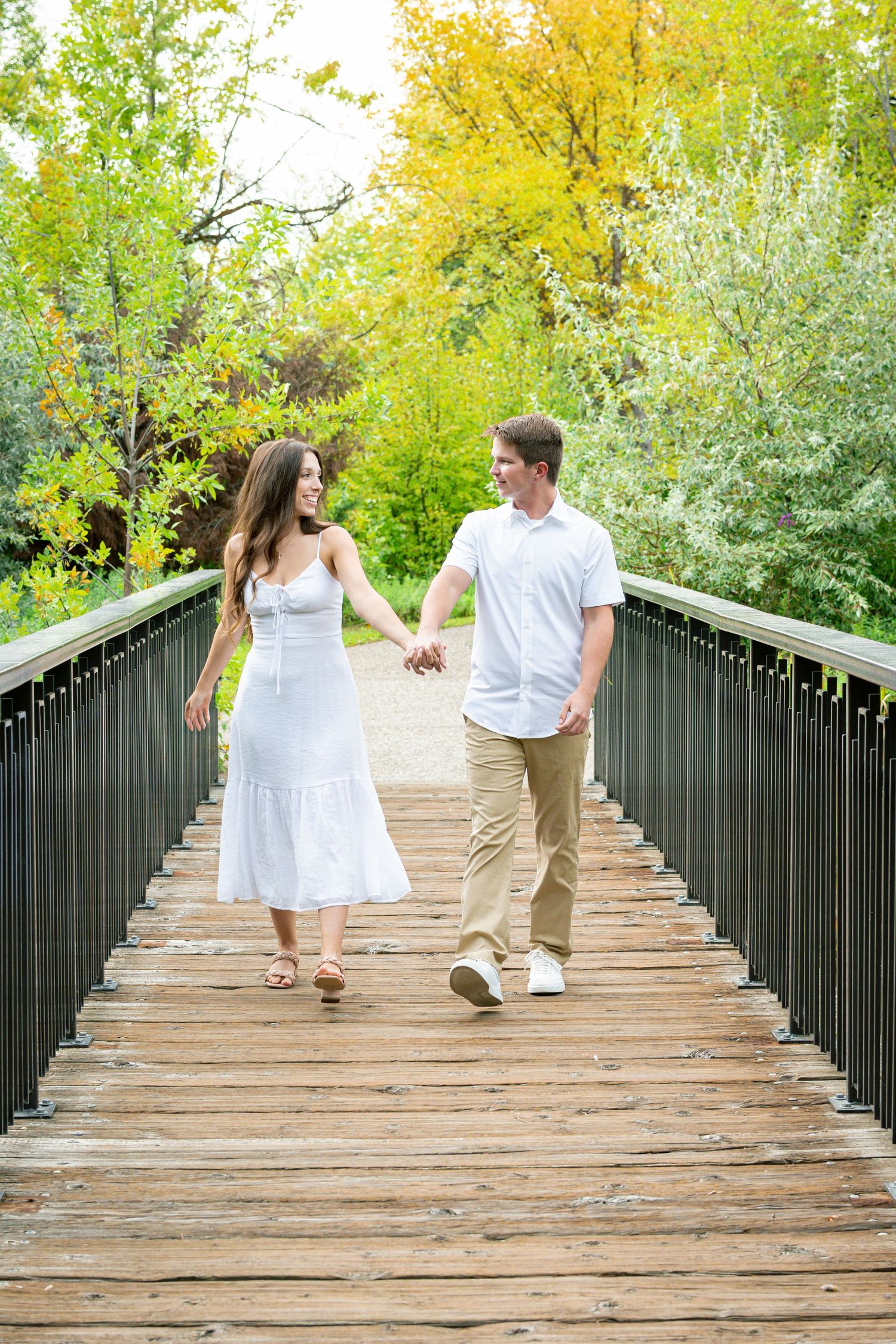Couple walking and holding hands on a wooden bridge surrounded by autumn foliage.