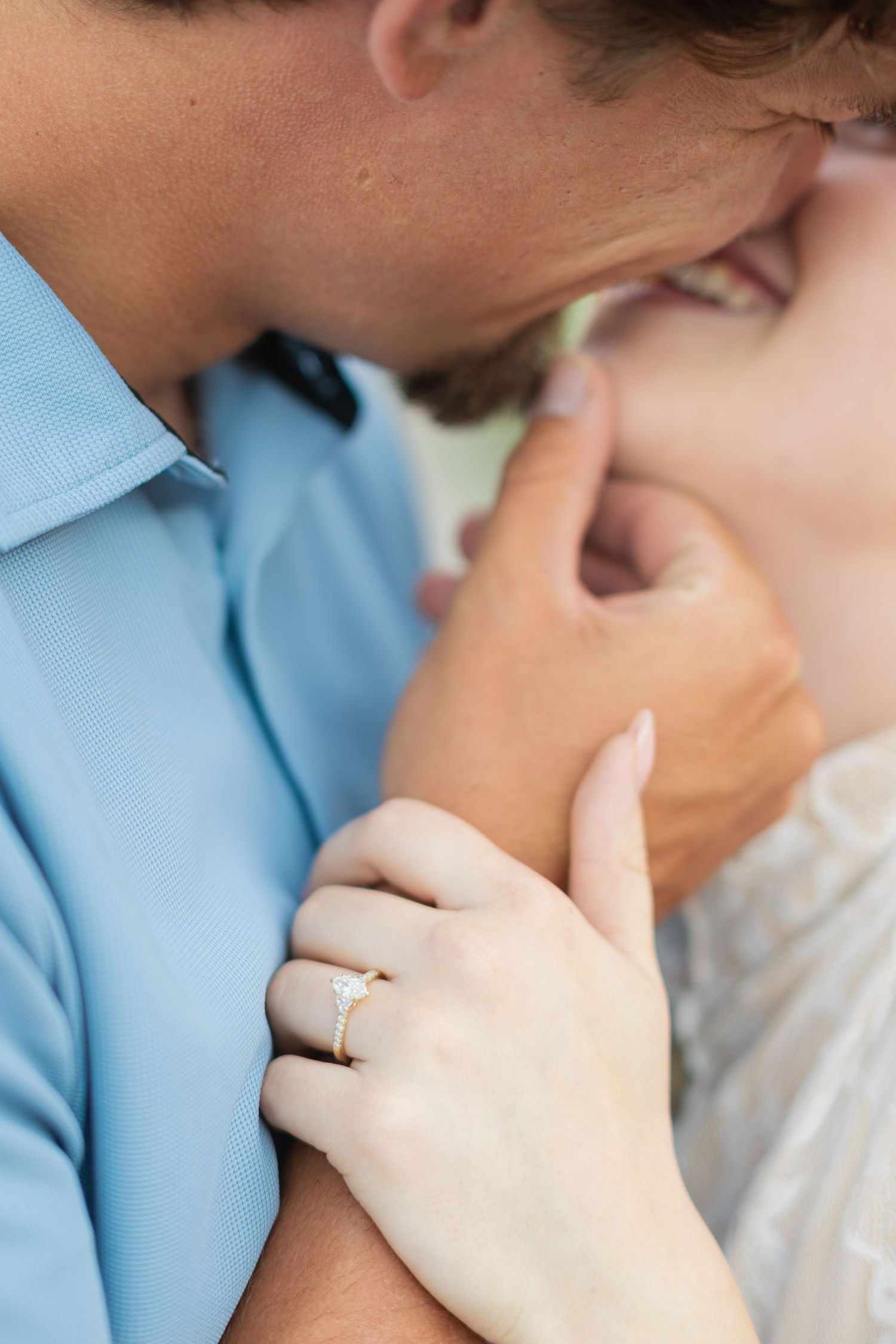 Close-up of couple almost kissing, woman wearing a delicate gold engagement ring, man in blue shirt.