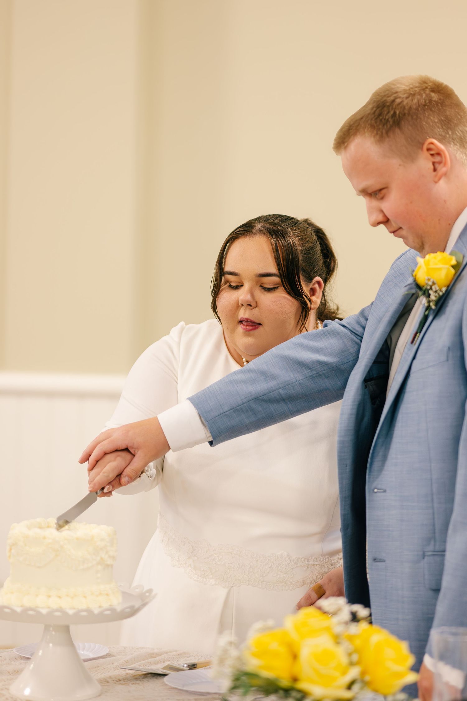 Wedding guests serve themselves at a buffet table decorated with yellow roses and white linens.