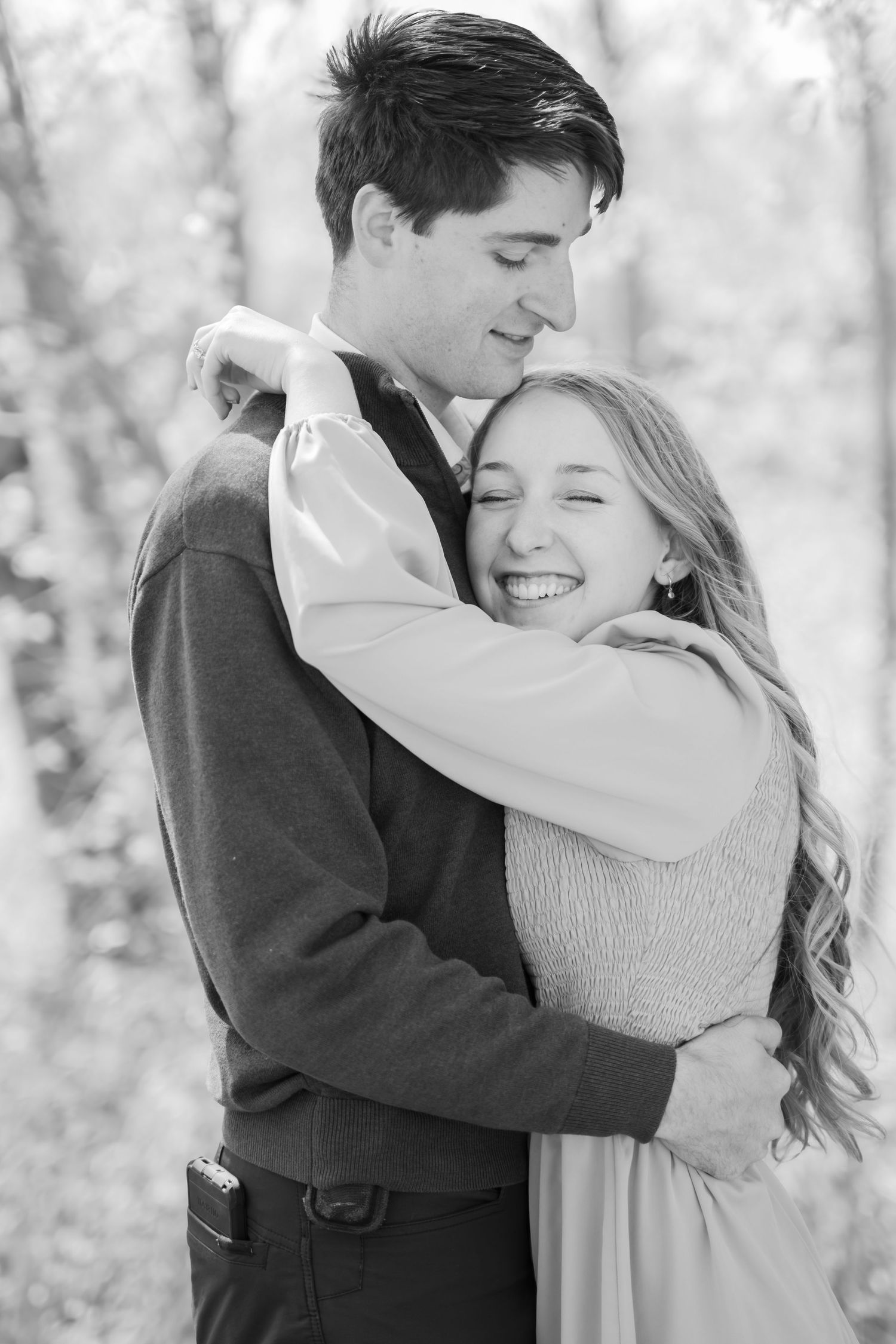 Black and white photo of a happy couple embracing outdoors, woman smiling joyfully while man looks down tenderly.