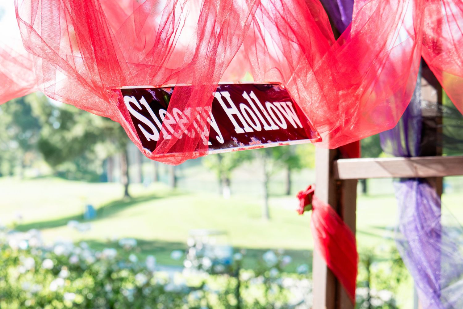 A decorative Sleepy Hollow sign hanging amid red and purple tulle fabric outdoors at a themed Halloween party event.