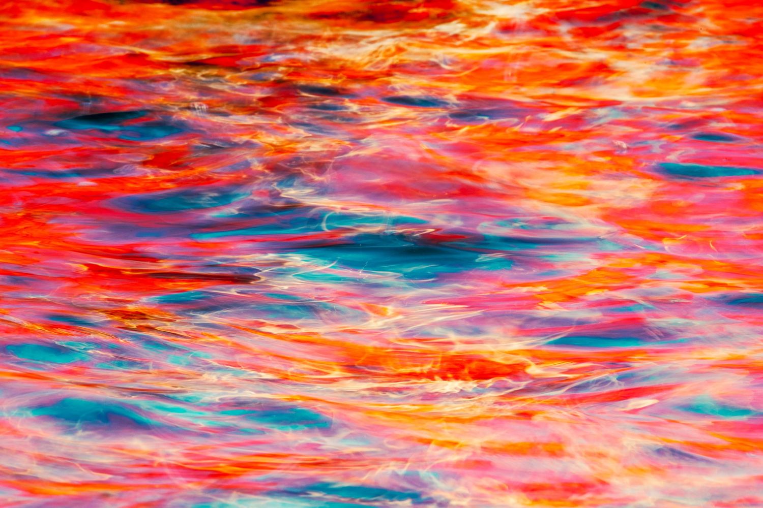 Vibrant red and orange reflections on rippling water surface create an abstract pattern.