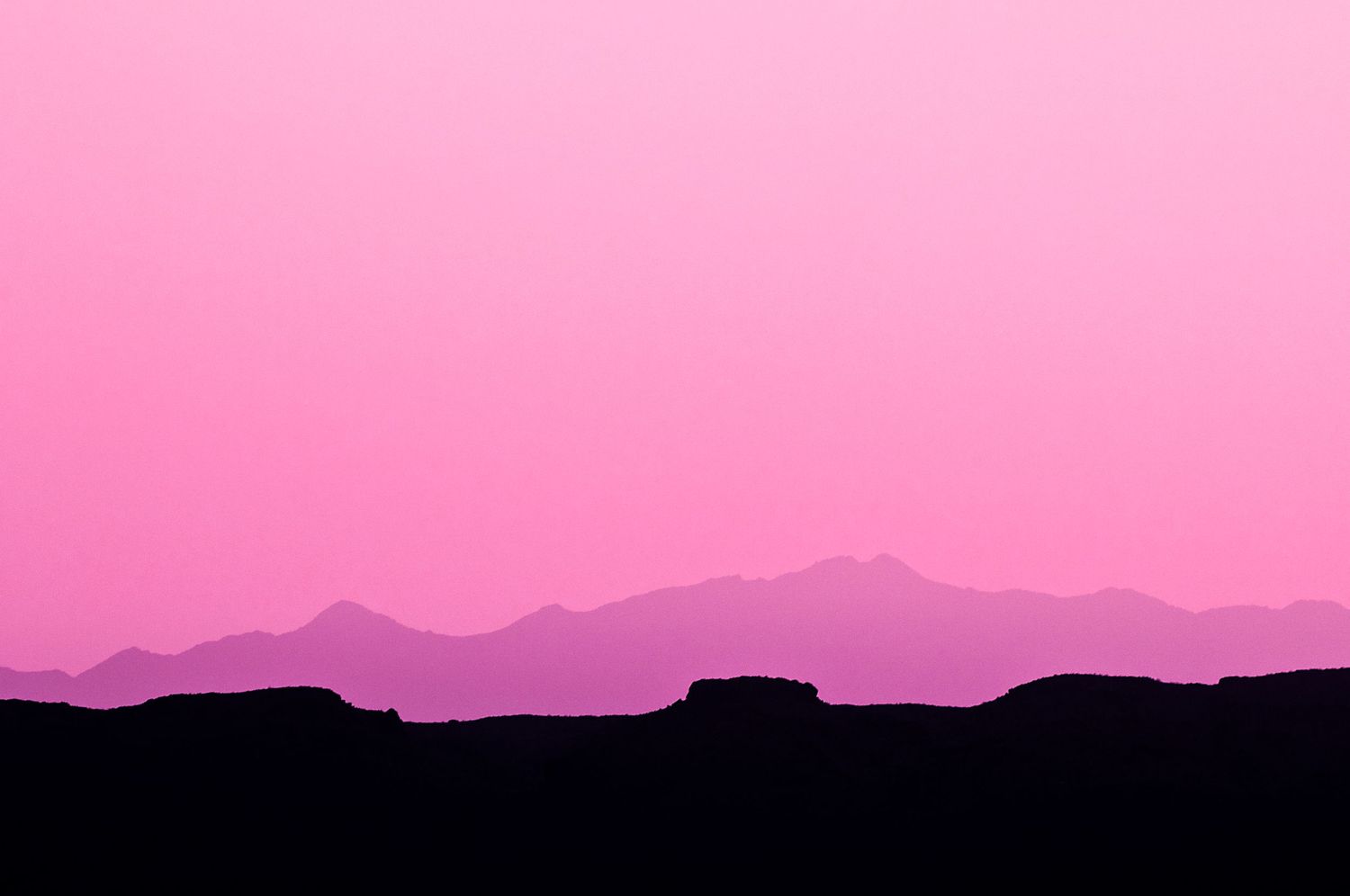 Mountain silhouettes against a vibrant pink sunset sky creating a layered landscape effect.