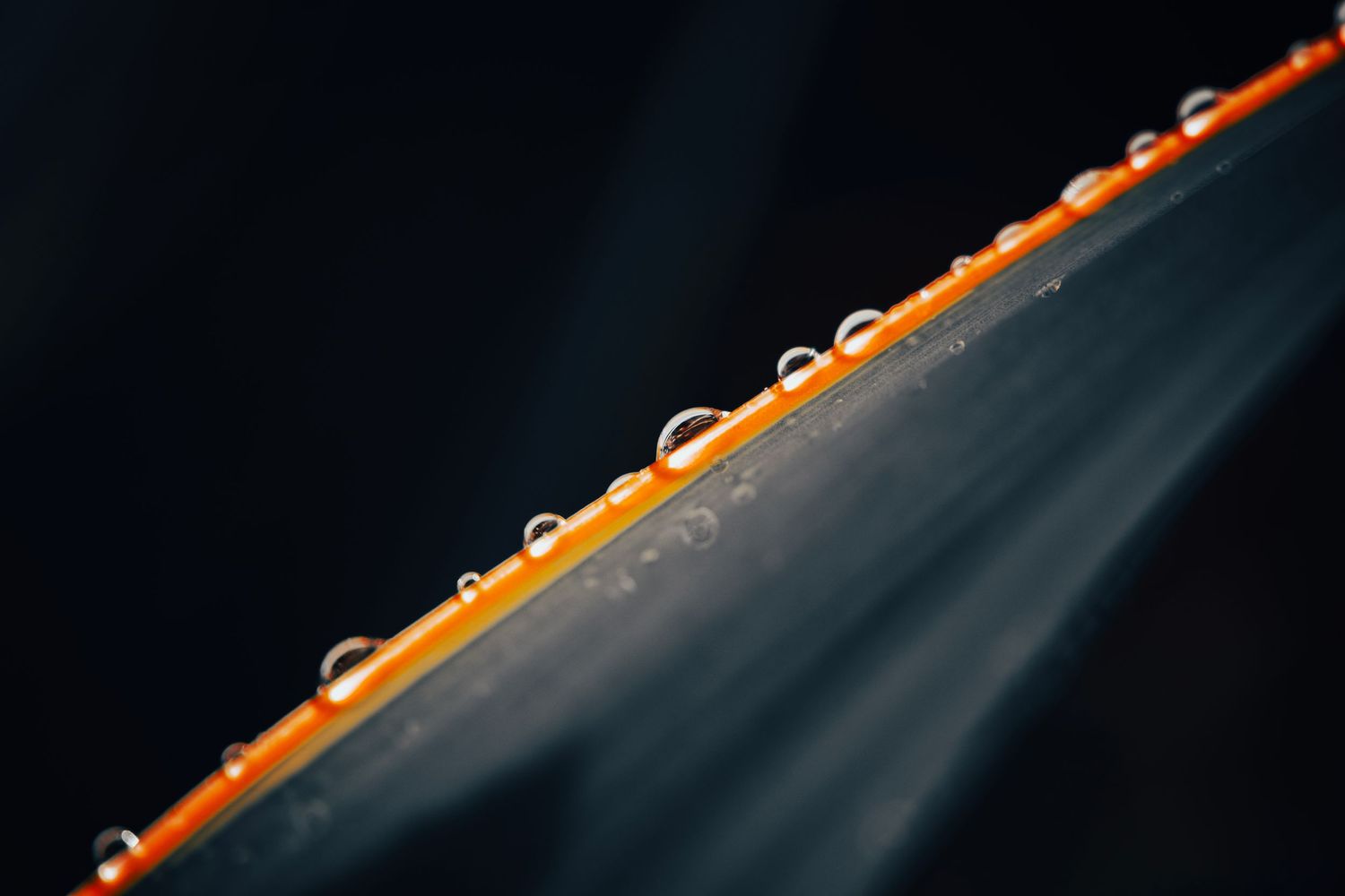 Water droplets line up along an orange surface against a dark background.