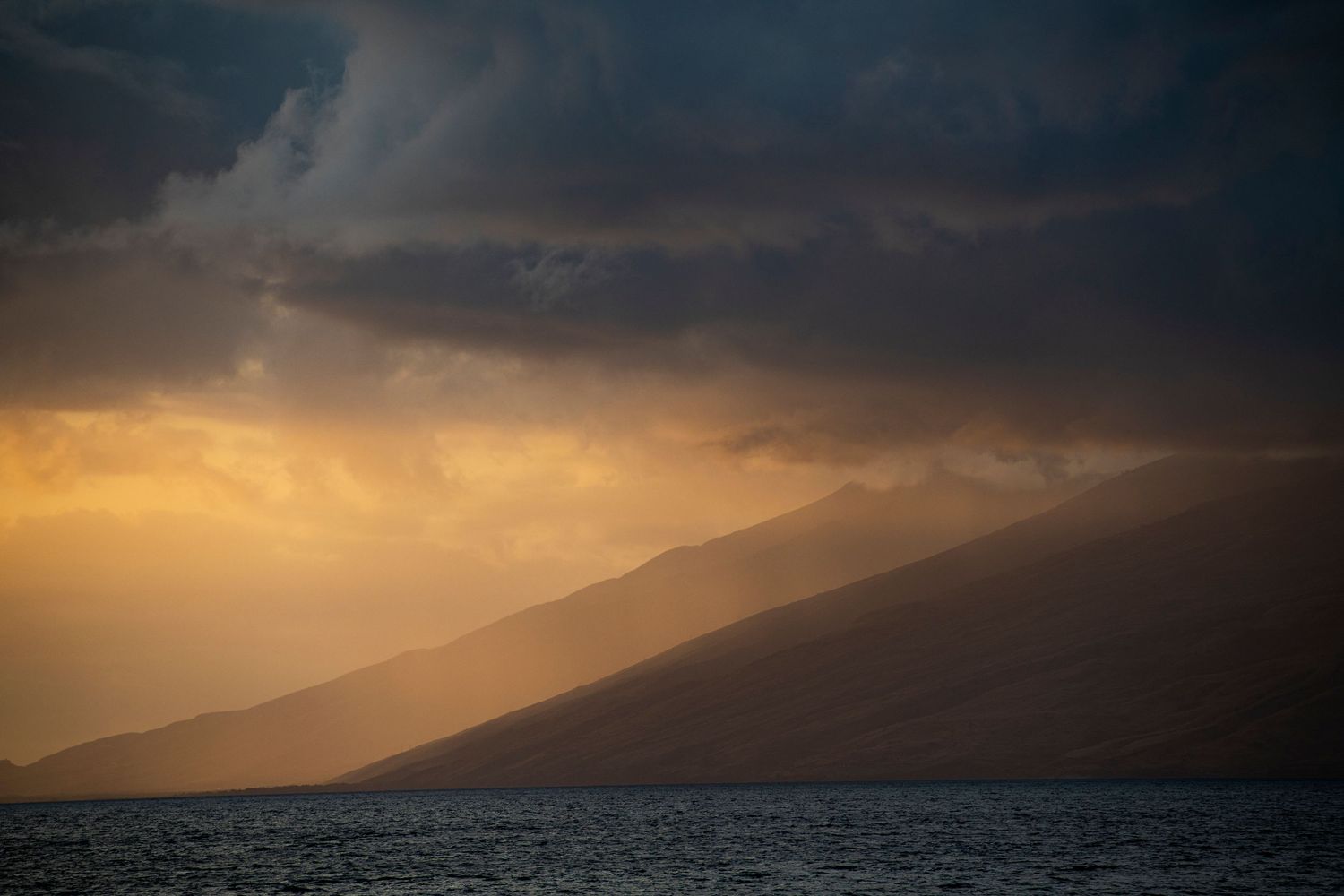 Dramatic mountain silhouette against a stormy sunset sky with dark clouds and golden light.