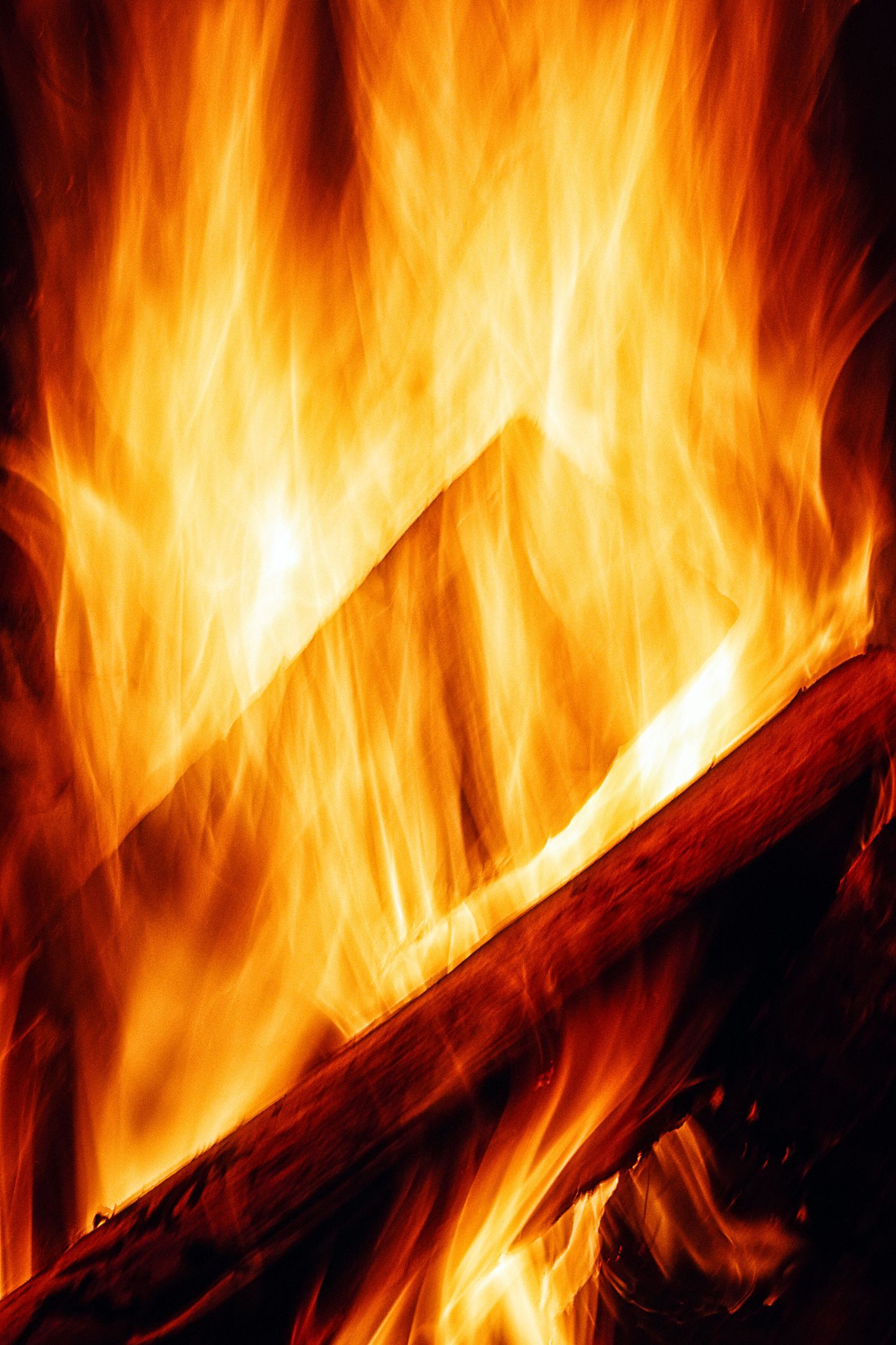 Bright orange flames engulf burning wood logs in a roaring fire, casting a warm and intense glow.