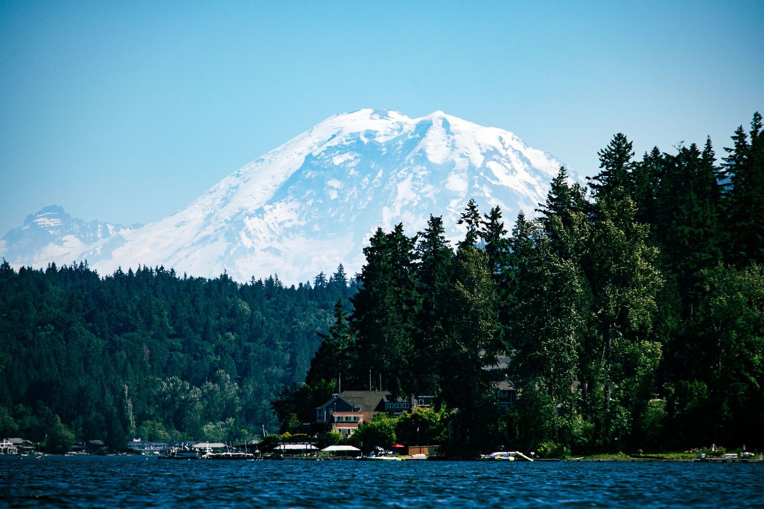 Snow-capped Mount Rainier rises above evergreen forests and lakeside homes.