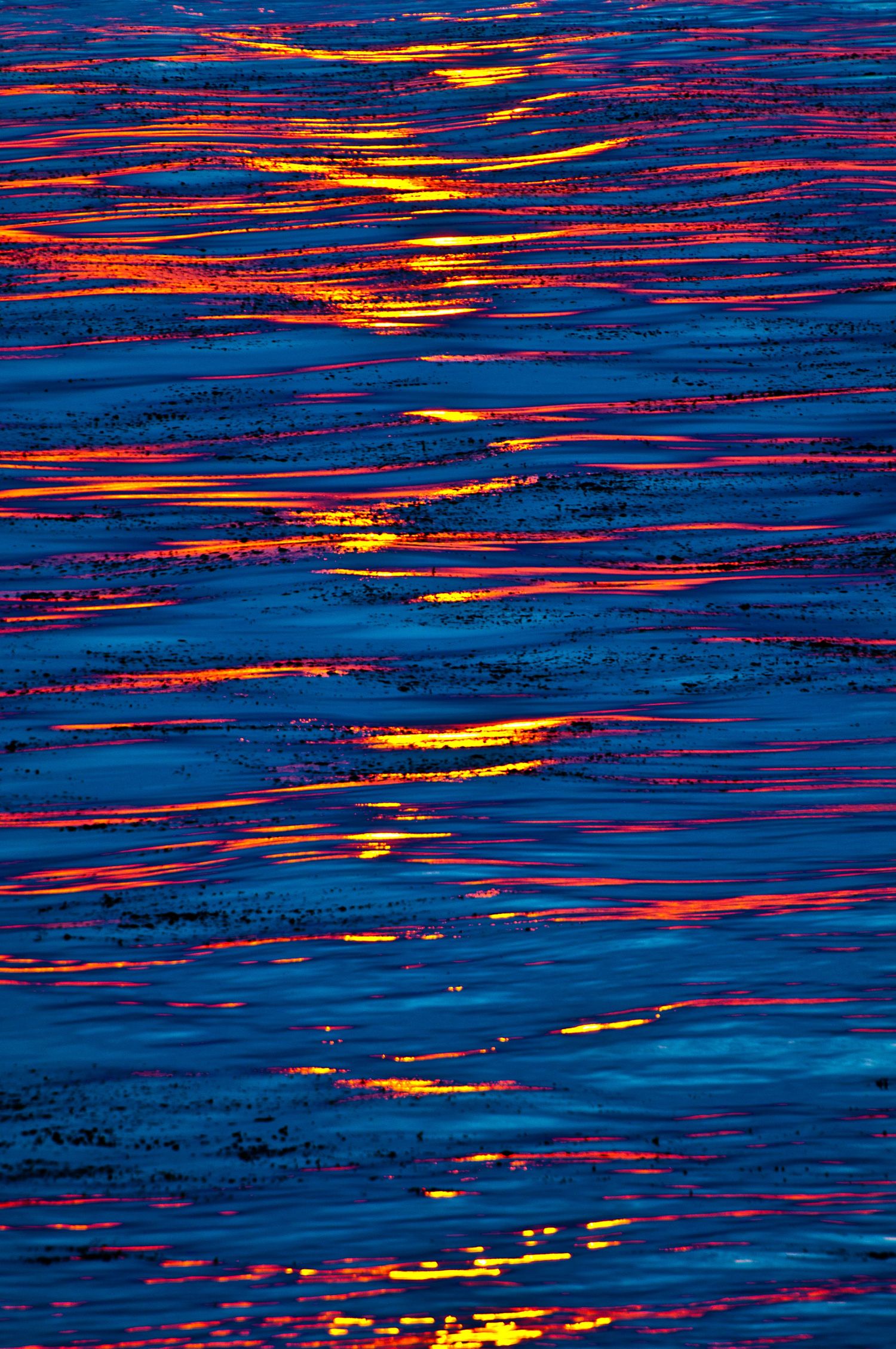 Abstract pattern of red and orange light reflections on dark blue water surface.