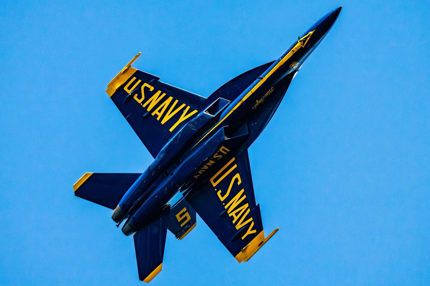 U.S. Navy Blue Angels F/A-18 Hornet jet performing an aerial maneuver against a clear blue sky.