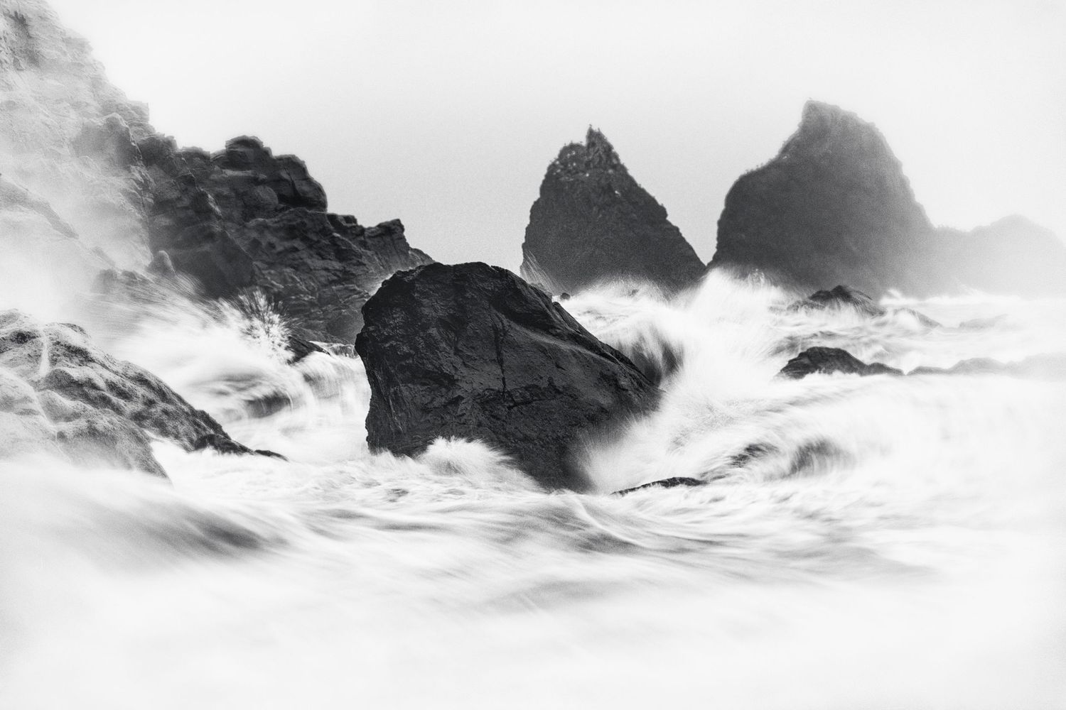 Dramatic black and white mountain peaks emerge through misty clouds in a moody panoramic landscape.