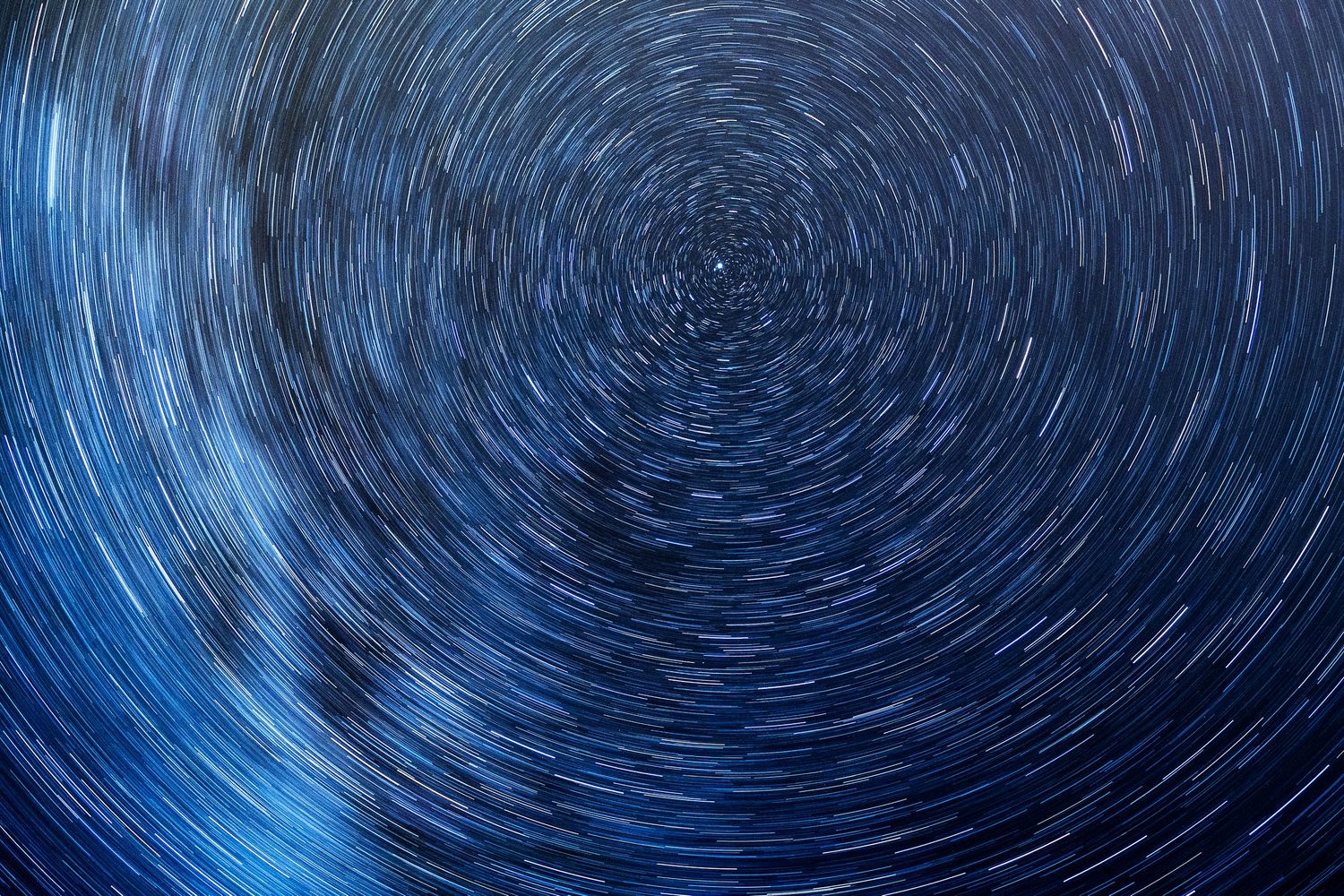 Long exposure night sky photograph showing circular star trails rotating around the North Star in deep blue hues.