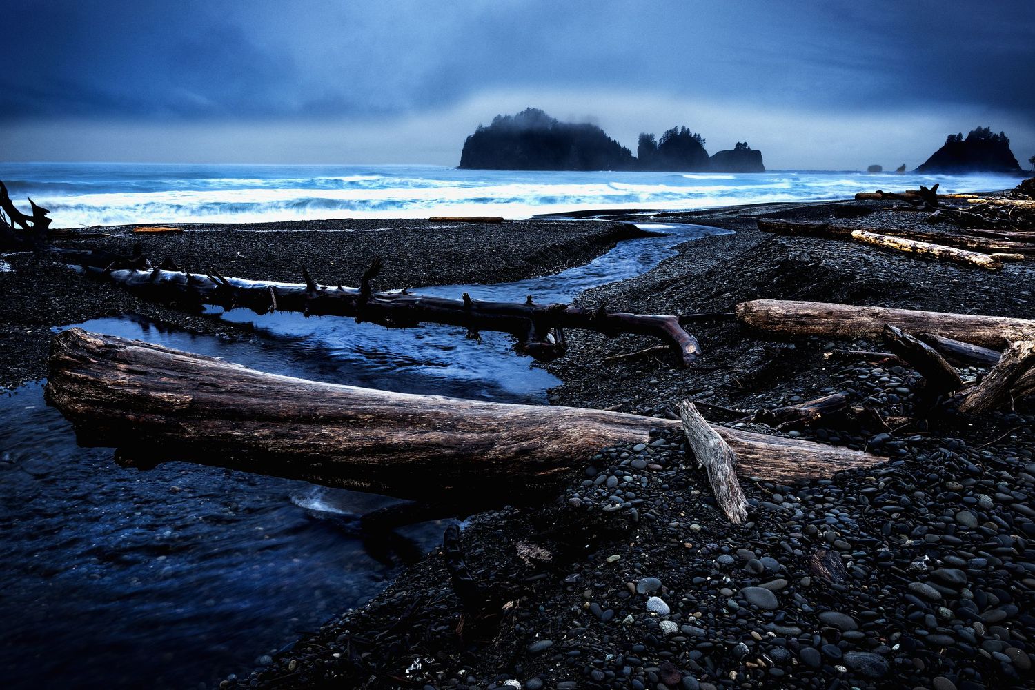 Dramatic panoramic view of rugged coastal cliffs and rocky shoreline under moody blue sky at dusk.