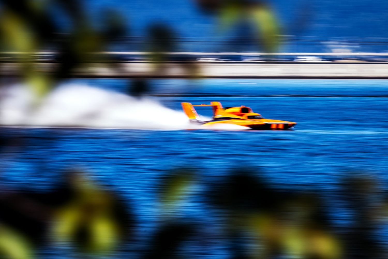 Orange hydroplane racing boat speeding across blue water, captured with motion blur effect at high-speed boat race.