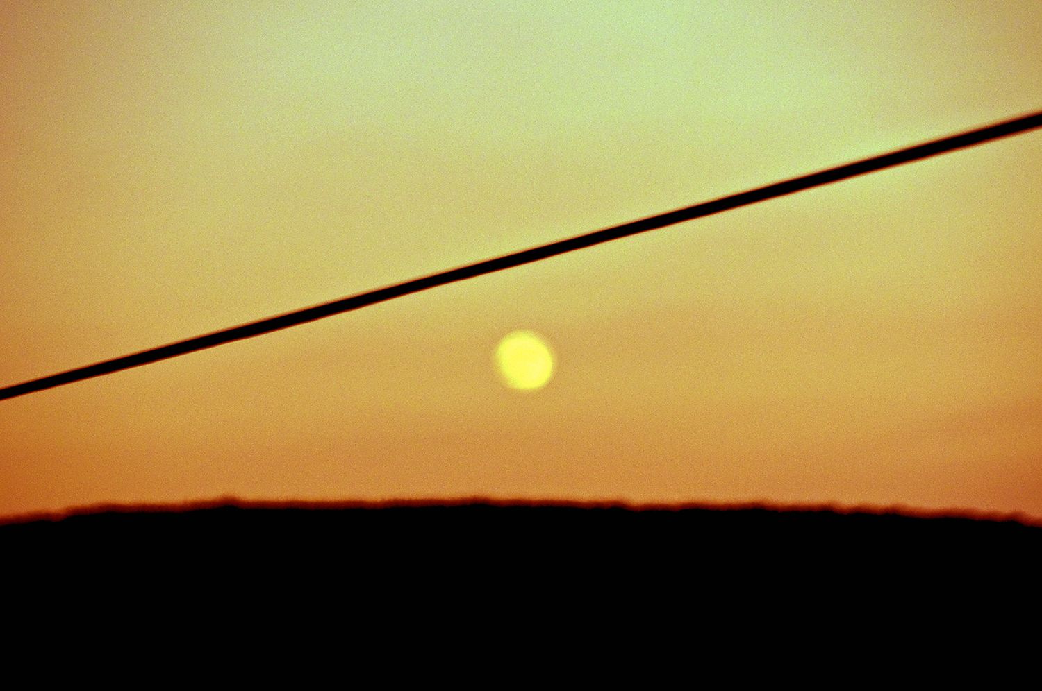 Minimalist sunset landscape with power lines silhouetted against orange sky.