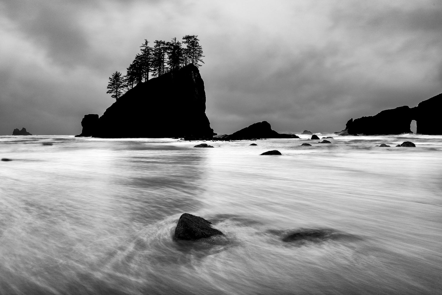 A dramatic black and white seascape with crashing waves and rocky outcrops along the Pacific Northwest coastline.