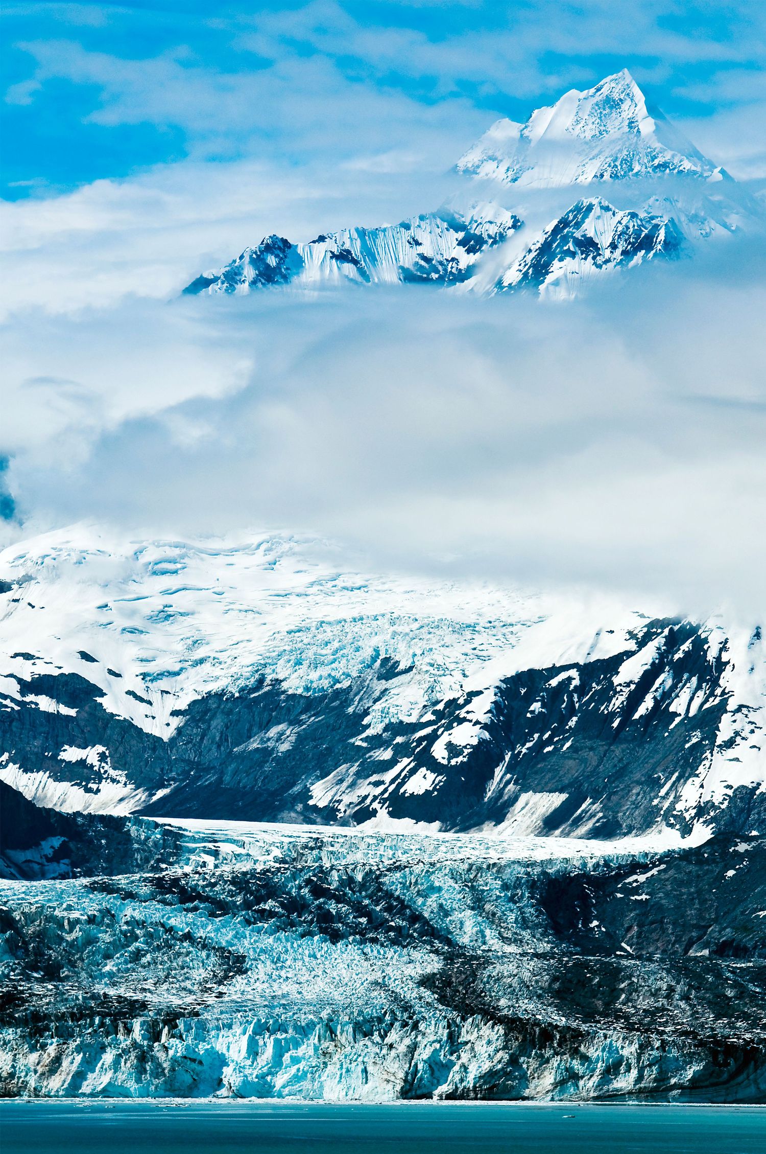 Massive glacier and snow-capped mountains reflect in pristine Alaskan waters.
